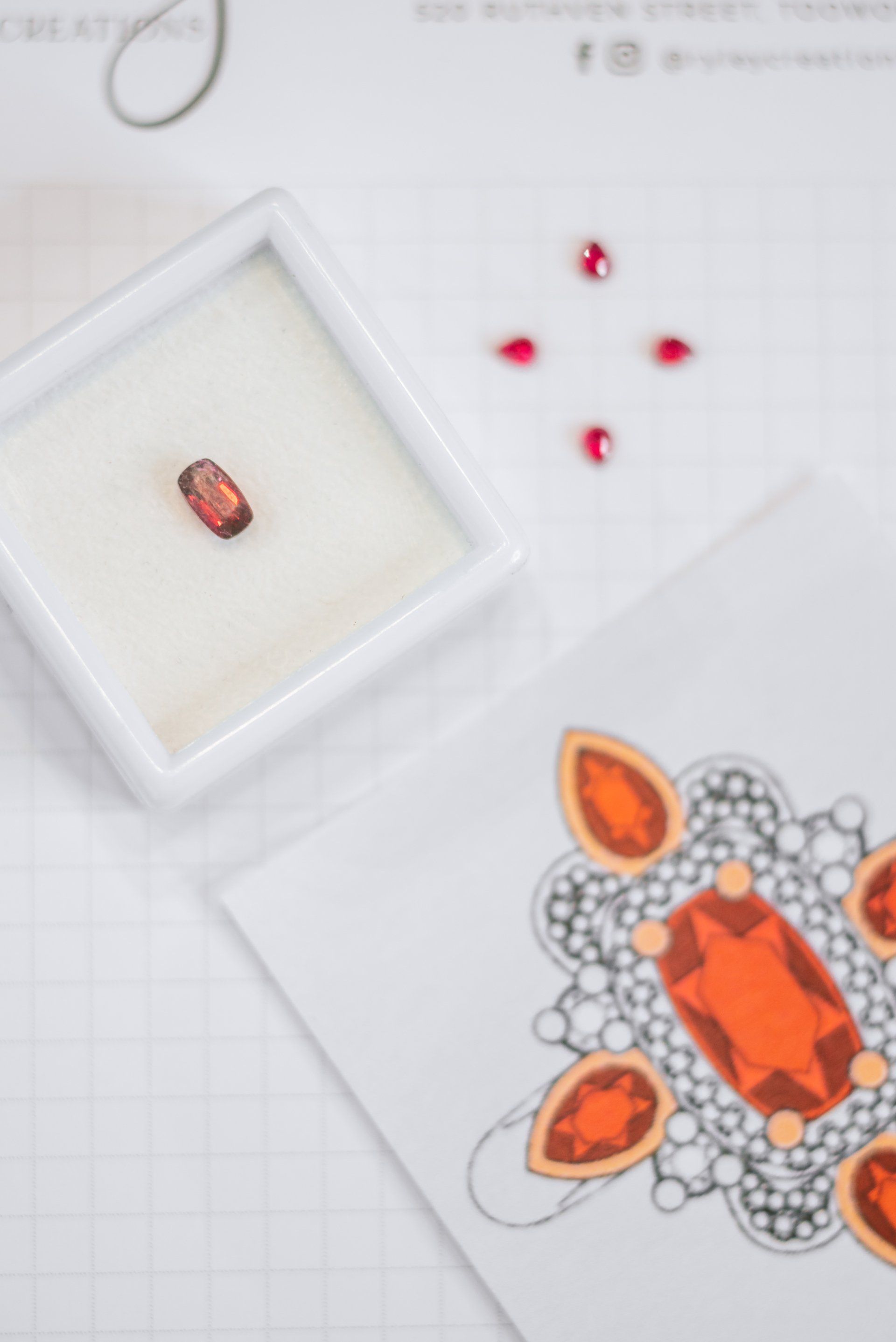 Jewelry design sketch with orange gemstone cluster, small red stones, and a tiny gem in a display tray