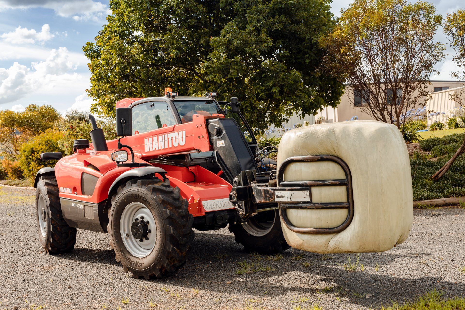 Red Manitou telehandler lifting a wrapped hay bale in a field