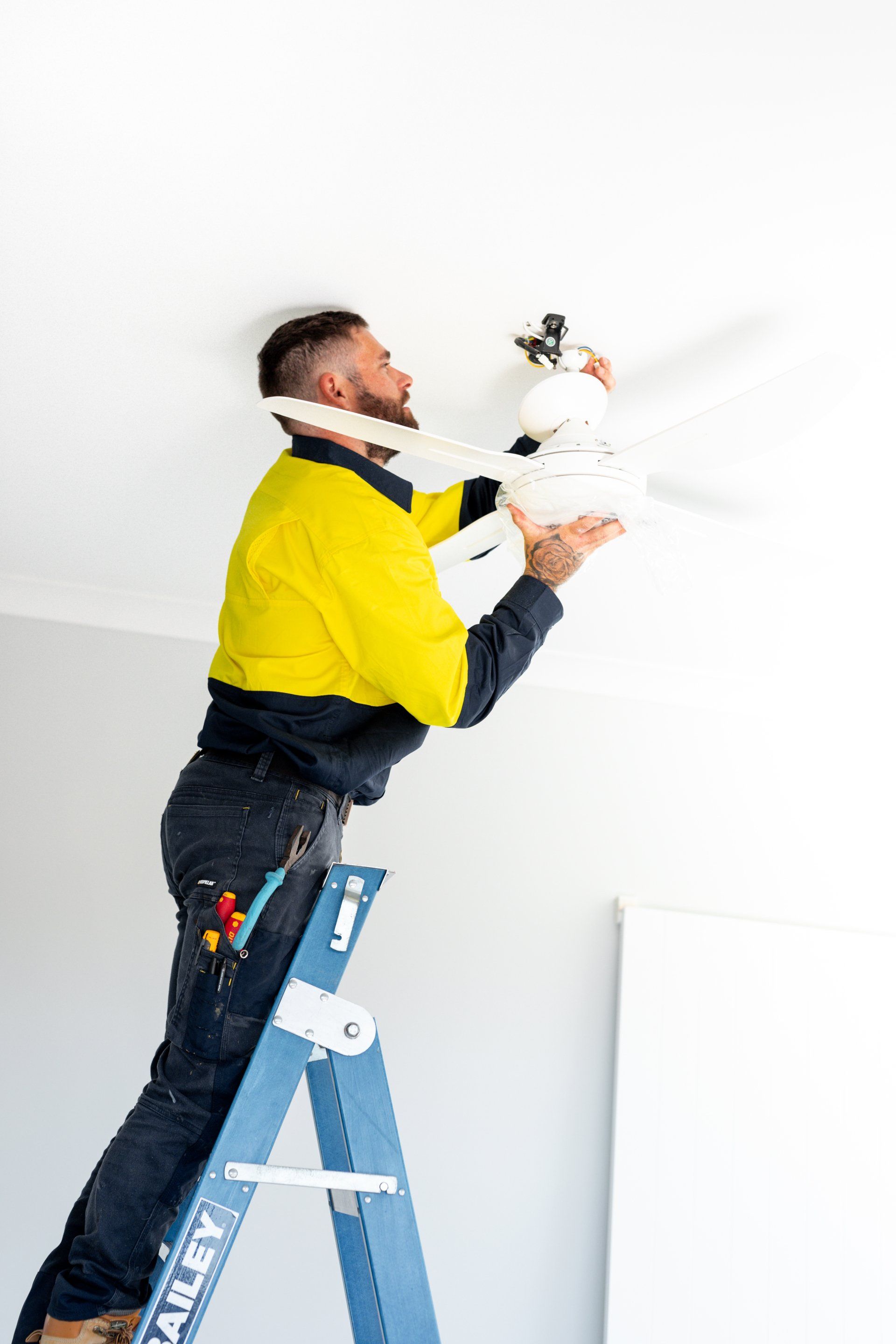 Worker on a blue ladder spray-painting a white ceiling with a paint sprayer