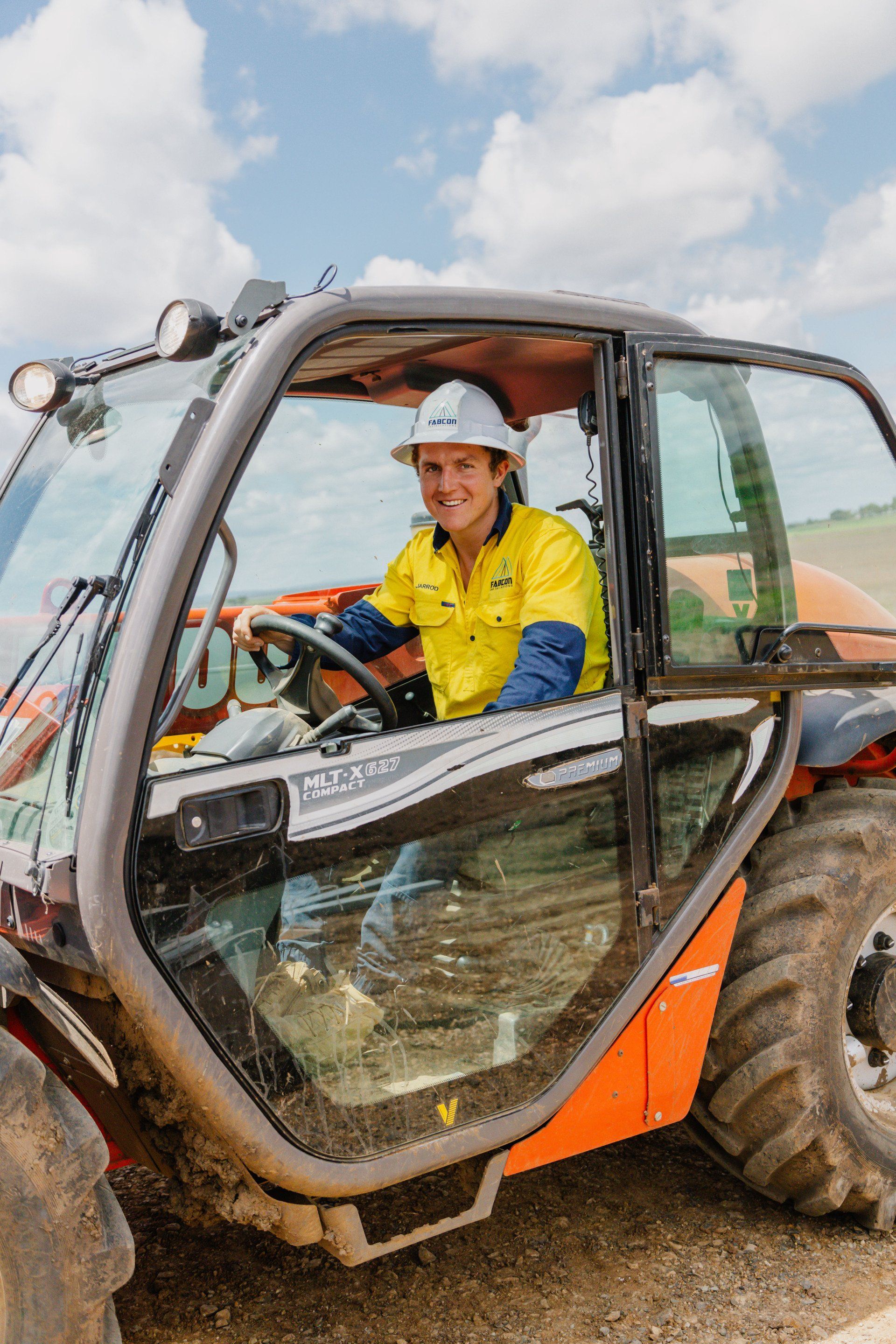 Person in yellow jacket driving a compact excavator on a muddy construction site