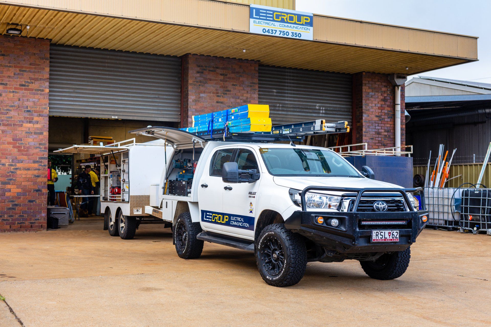 White utility truck with blue and yellow equipment parked outside a brick warehouse