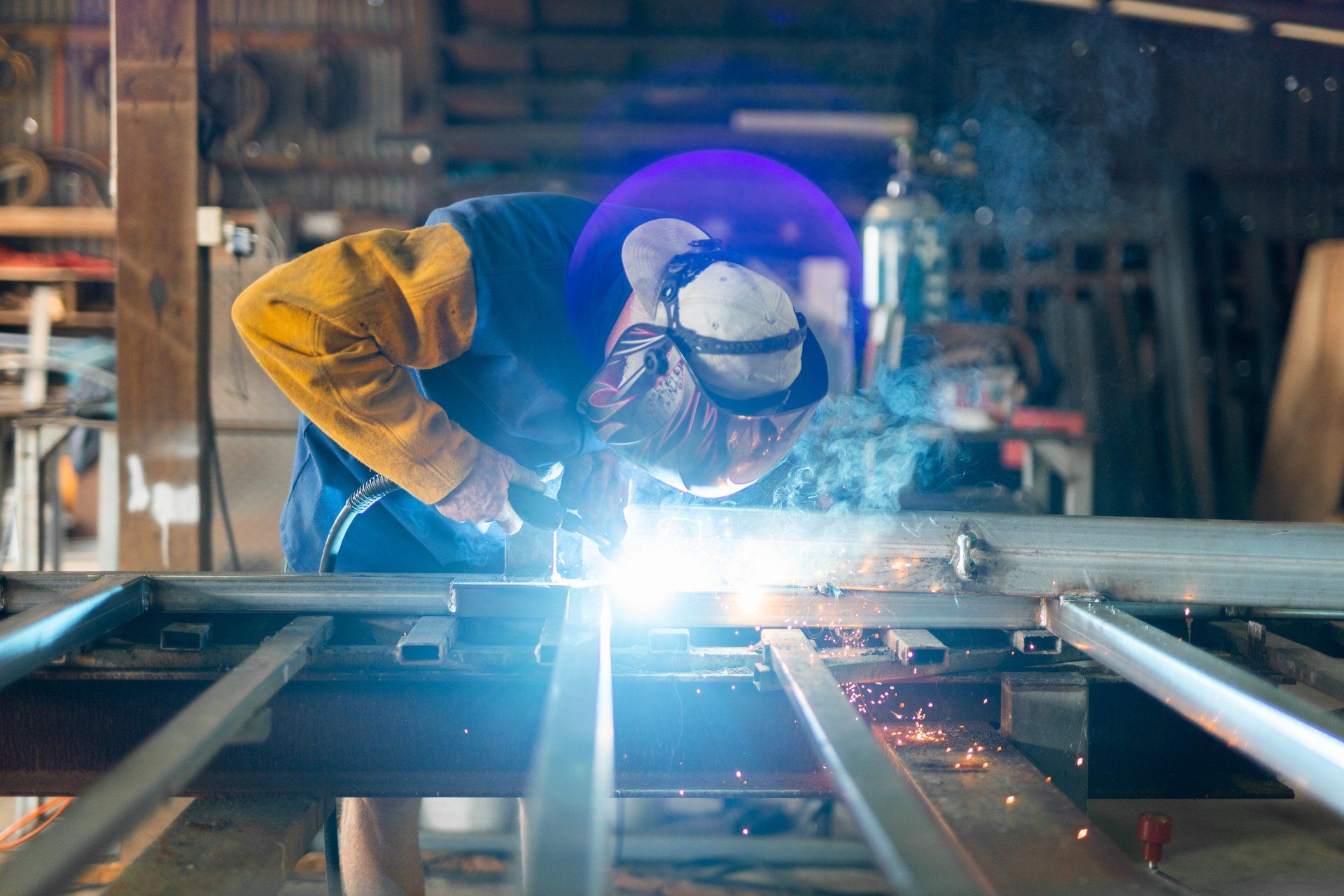 Welder in protective gear working on metal frame with bright sparks in an industrial workshop