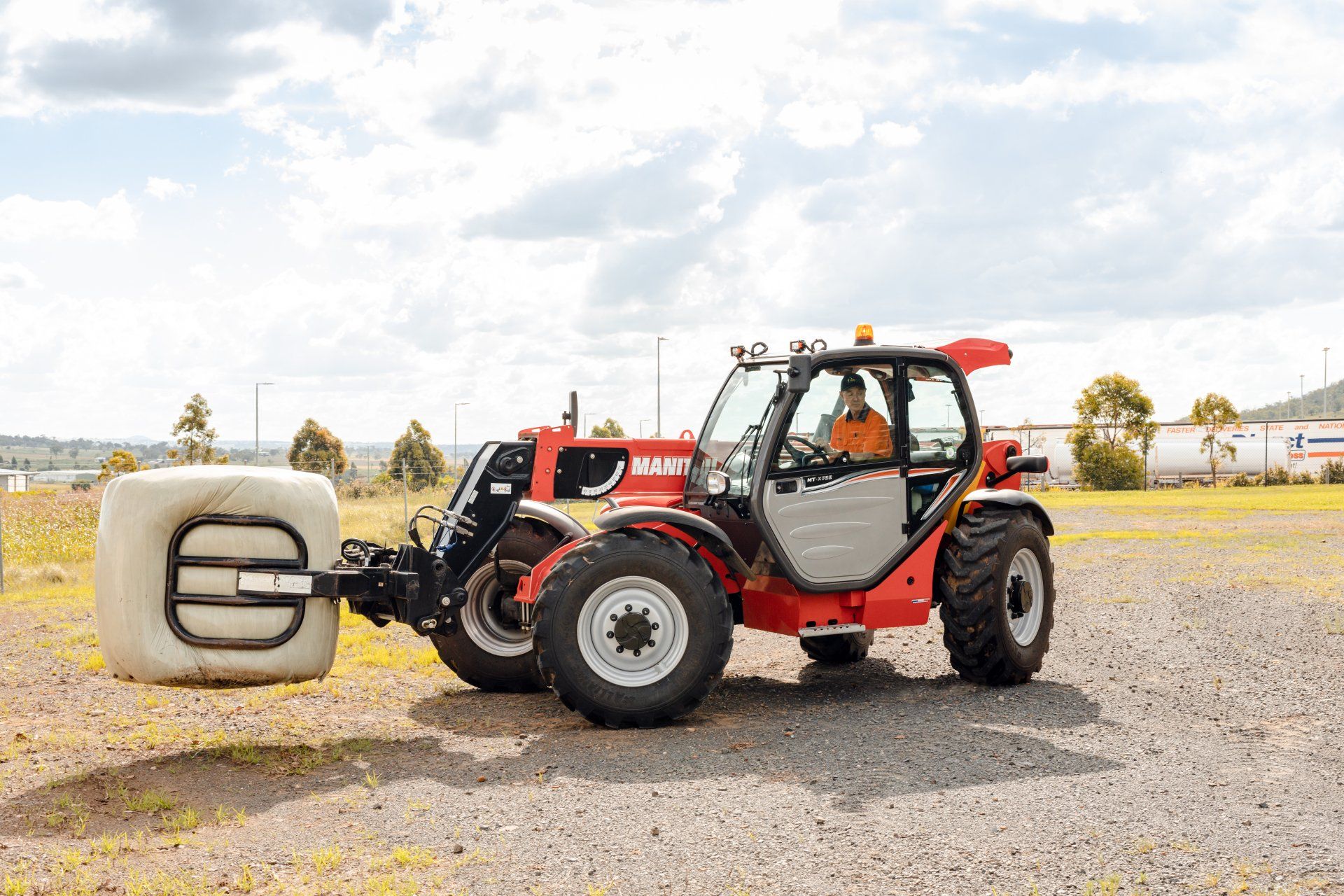 Red forklift with large bale clamp on gravel lot under cloudy sky