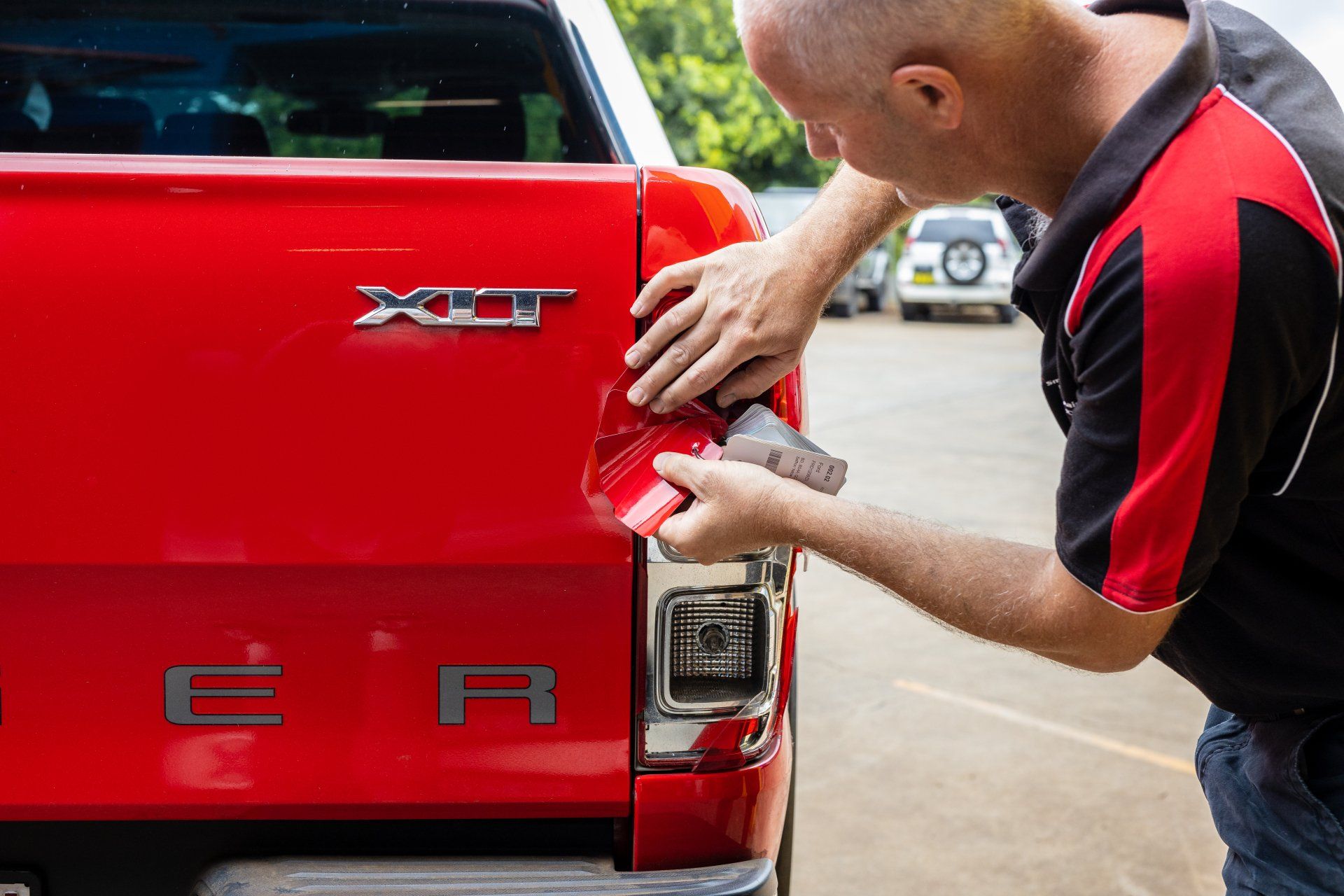 Man applying a badge to the rear of a red pickup truck