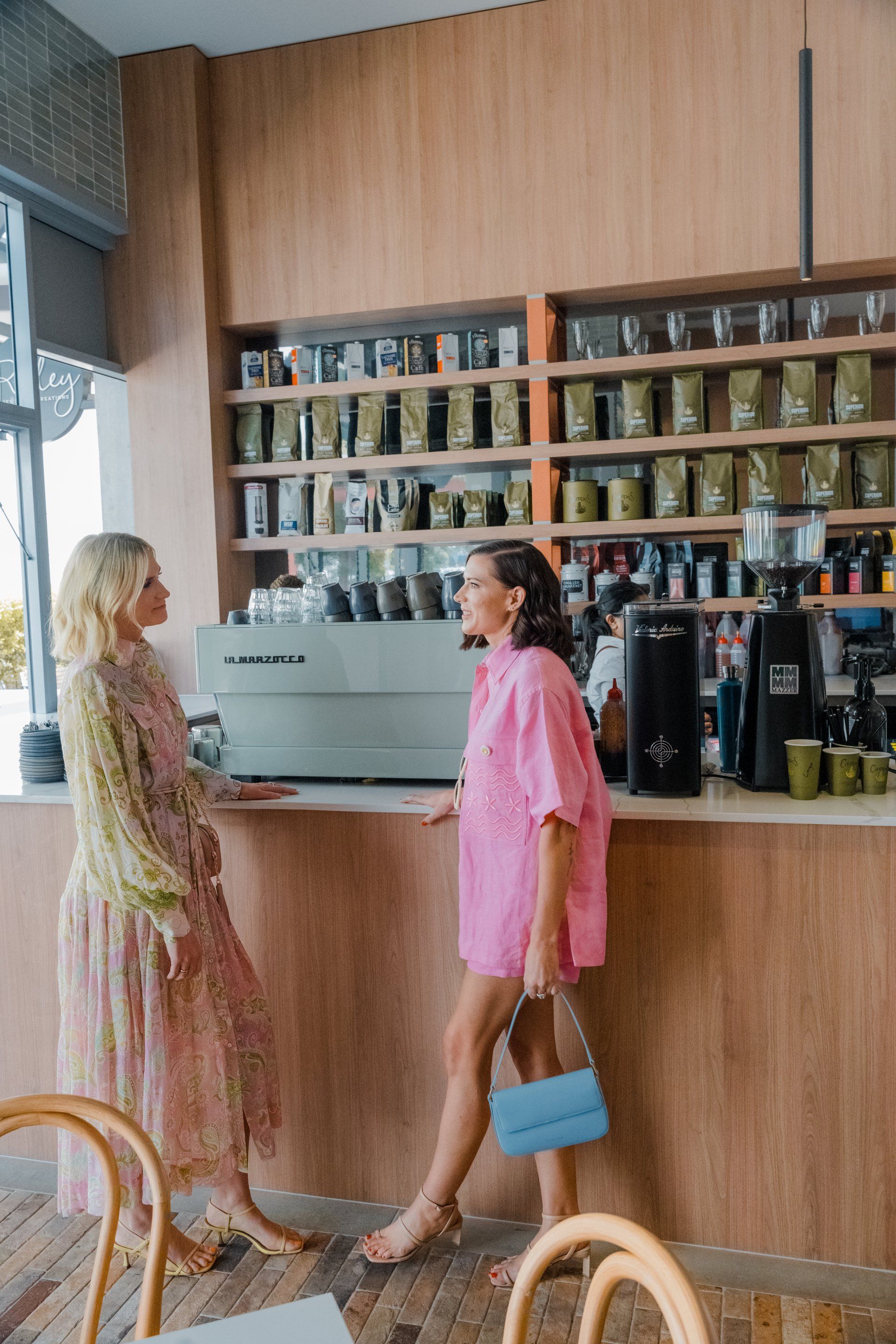 Two people talking at a coffee shop counter with shelves of jars behind them
