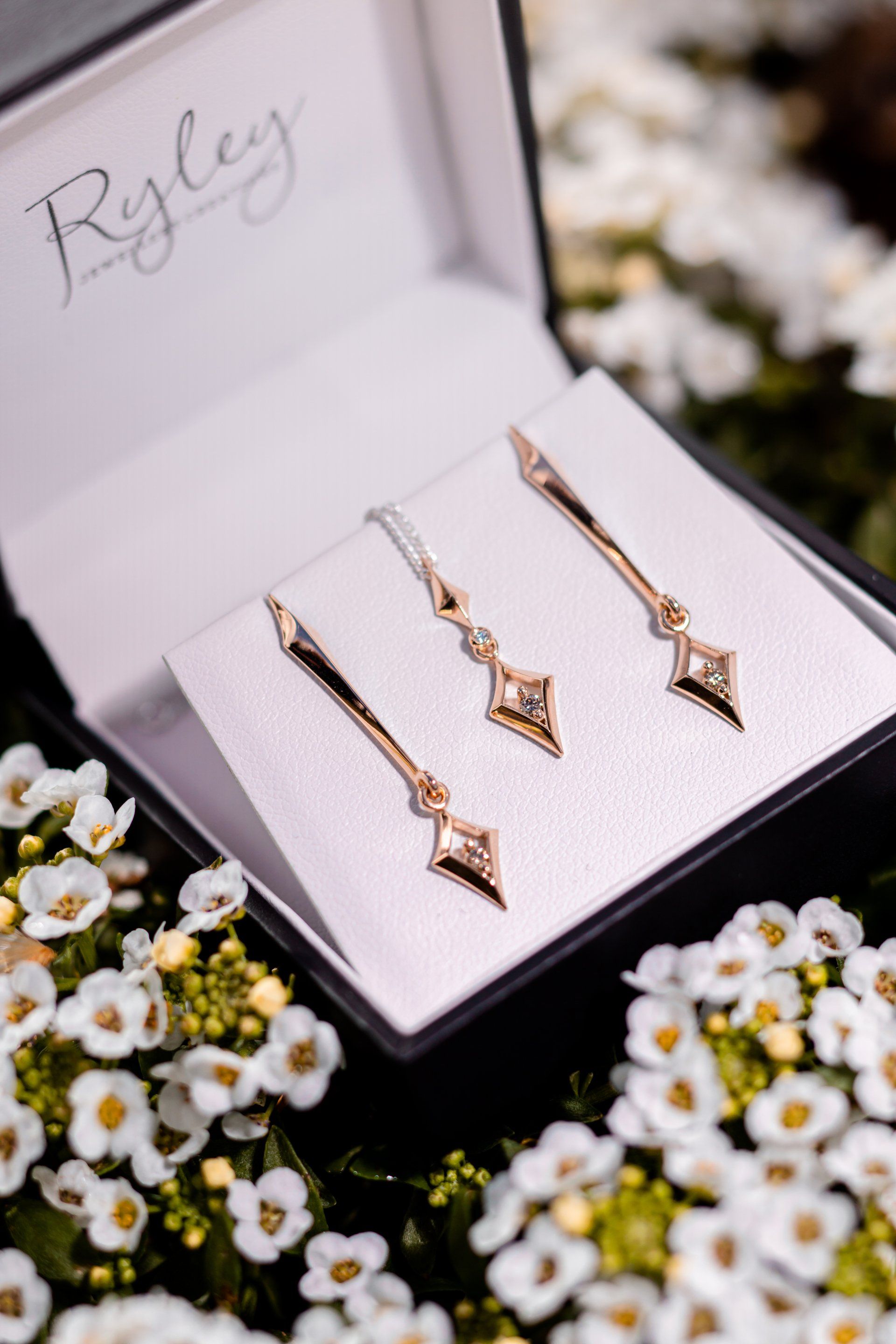 Rose gold arrow earrings in a white gift box, surrounded by small white flowers.