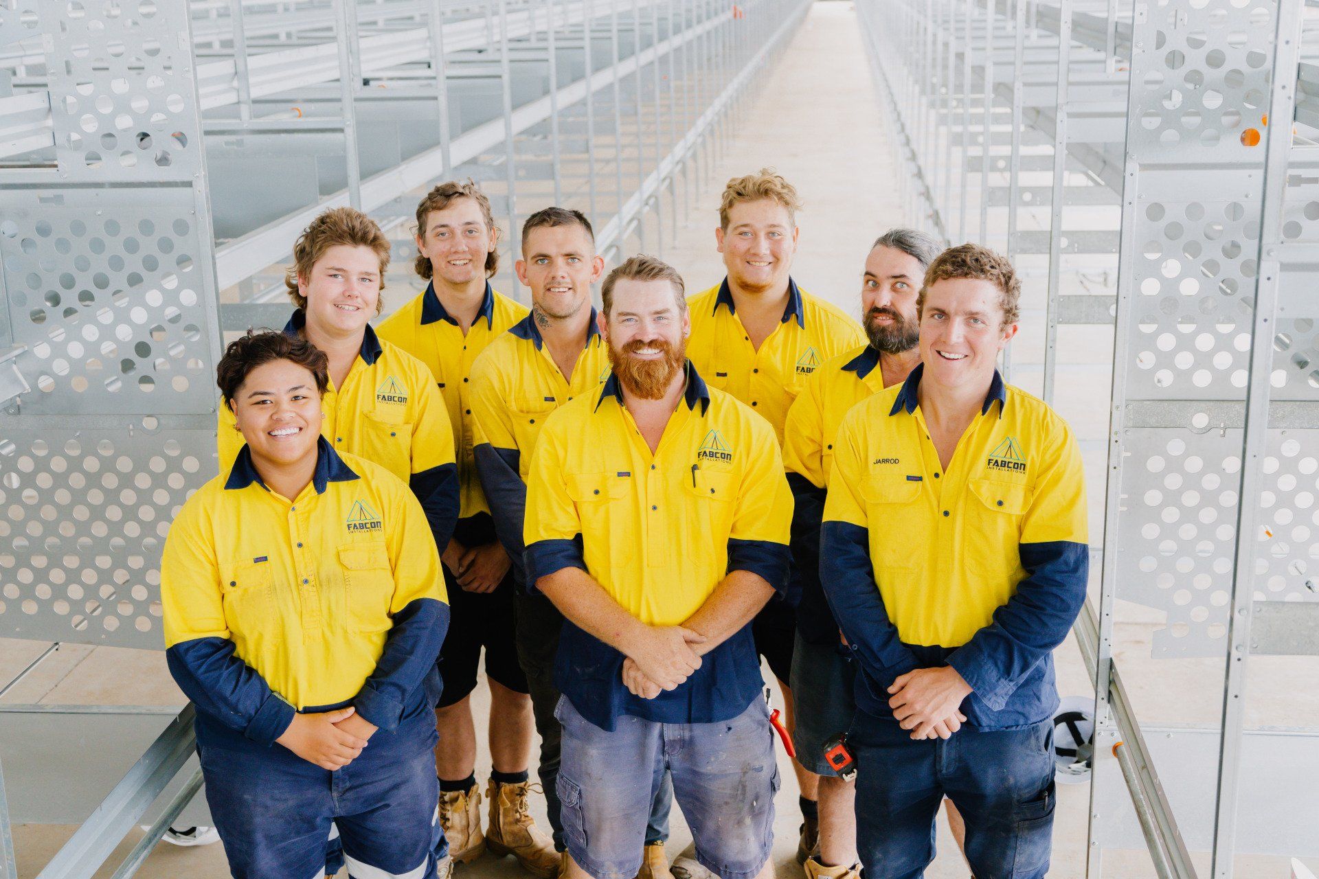 Group of workers in yellow shirts standing in a bright industrial warehouse aisle