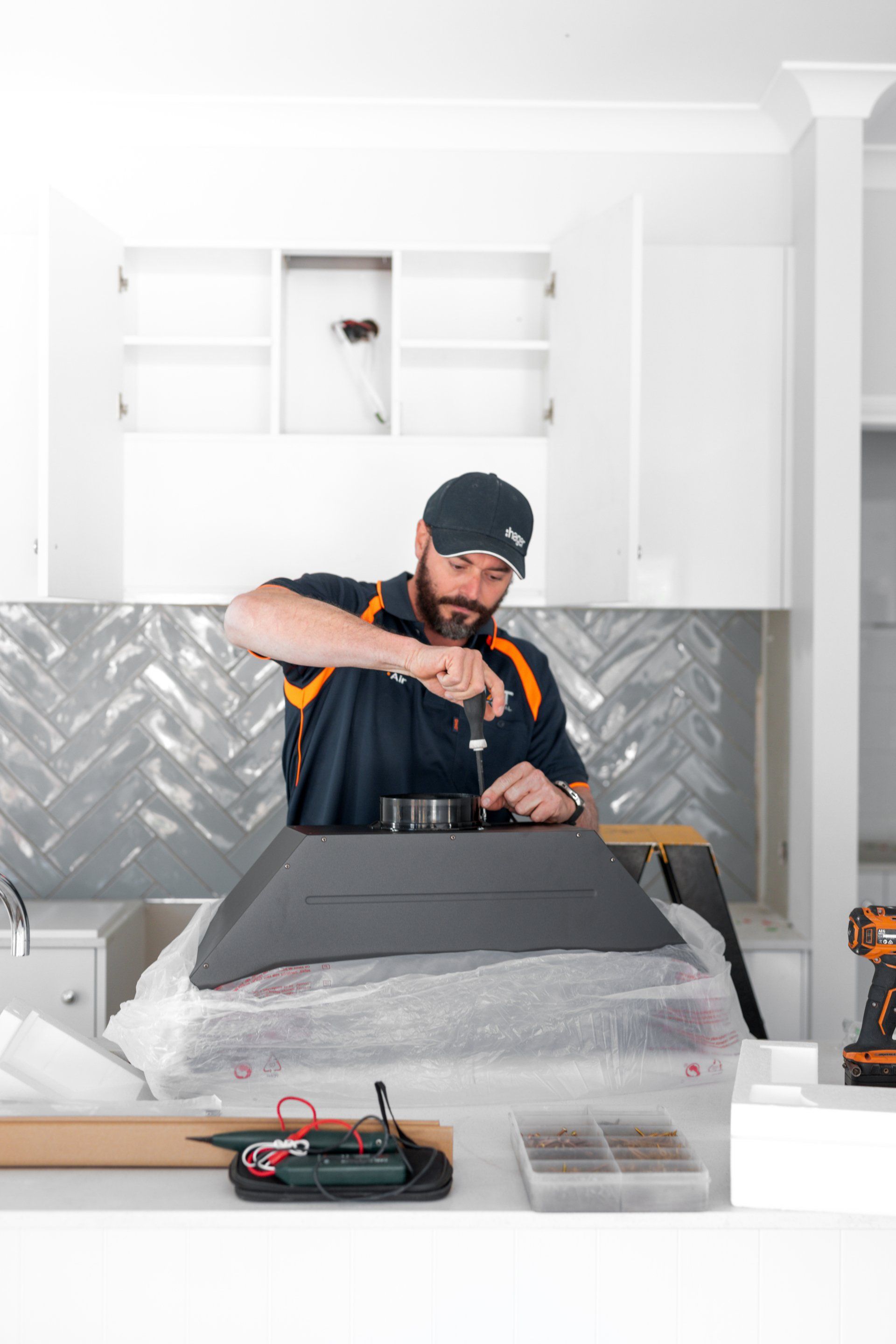Person working on a kitchen backsplash installation with tools and tile materials in a white kitchen.