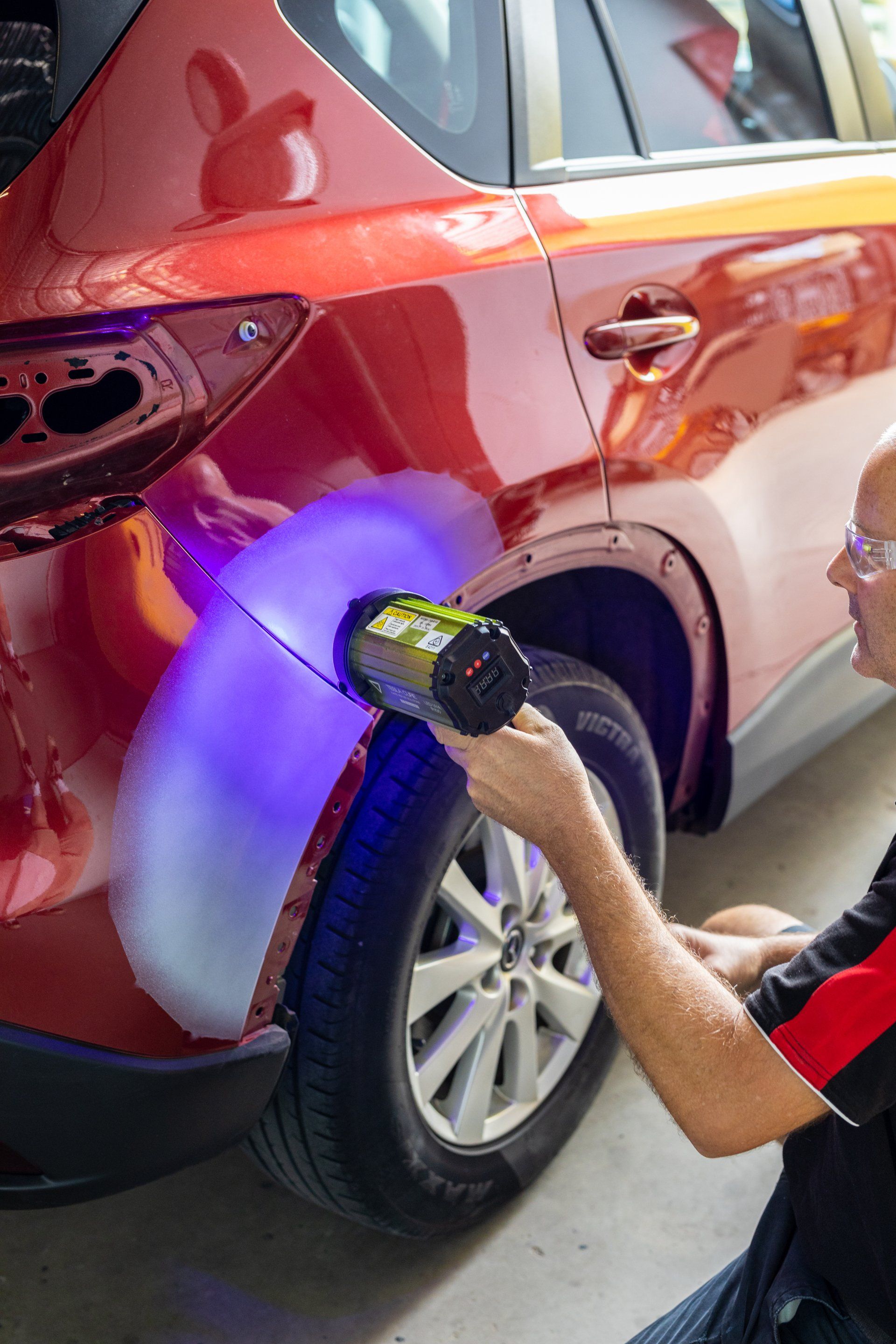 Person using a UV flashlight to inspect the rear quarter panel of a red car in a garage