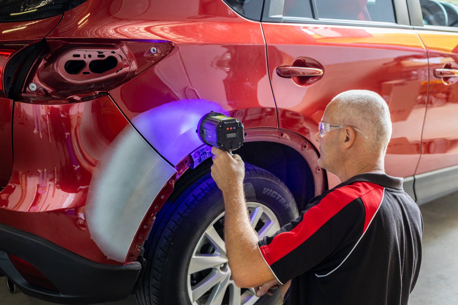 Technician inspecting a red SUV’s rear wheel with a handheld scanner under purple light