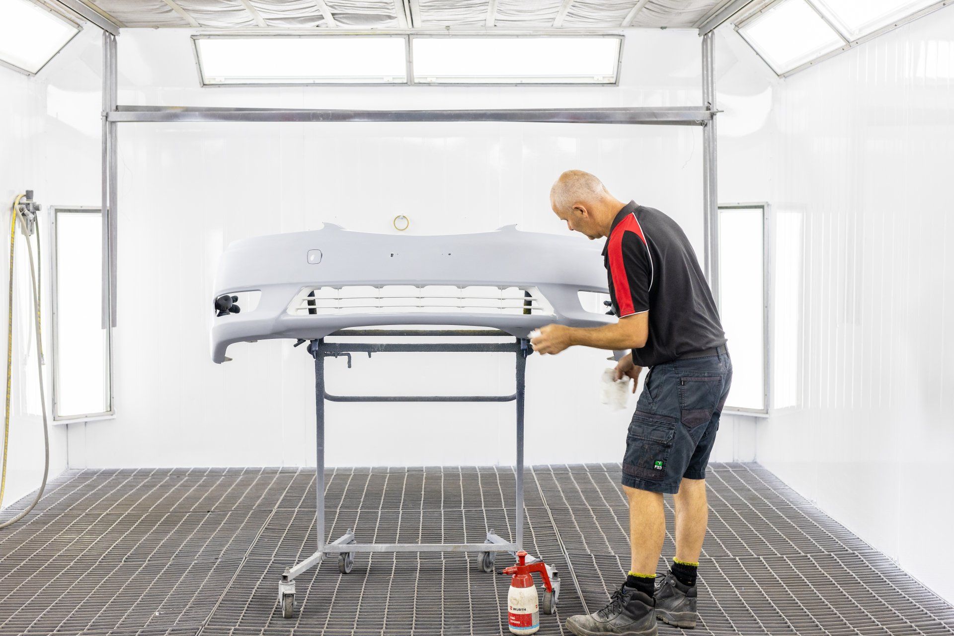 Person inspecting a car bumper in a bright auto spray booth