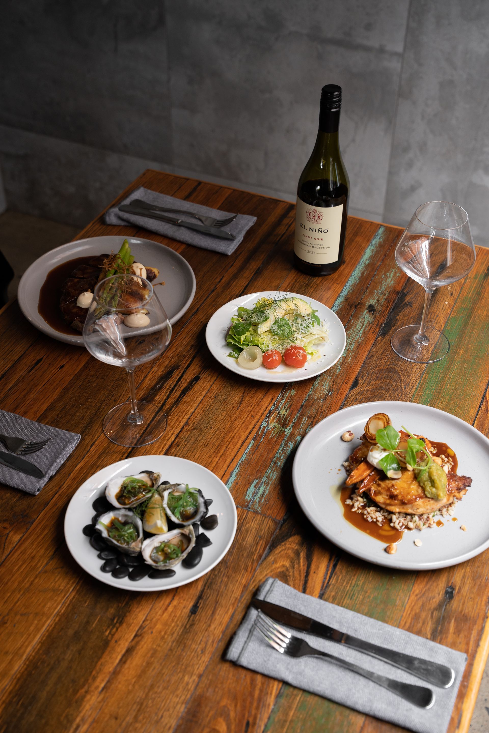 Restaurant table with plated dishes, wine bottle, and glasses on a rustic wooden table
