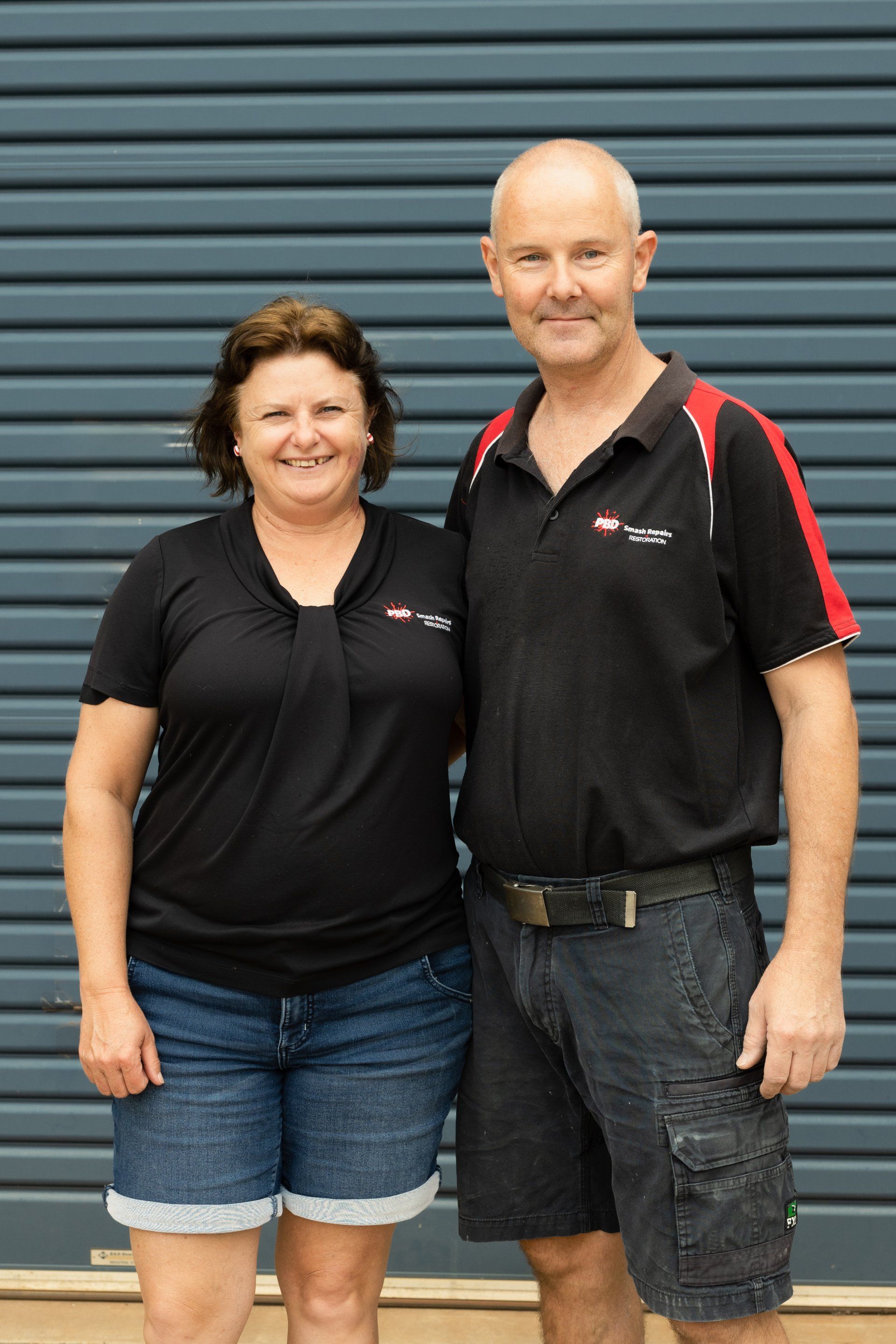 Two people in black polo shirts standing in front of a blue metal wall