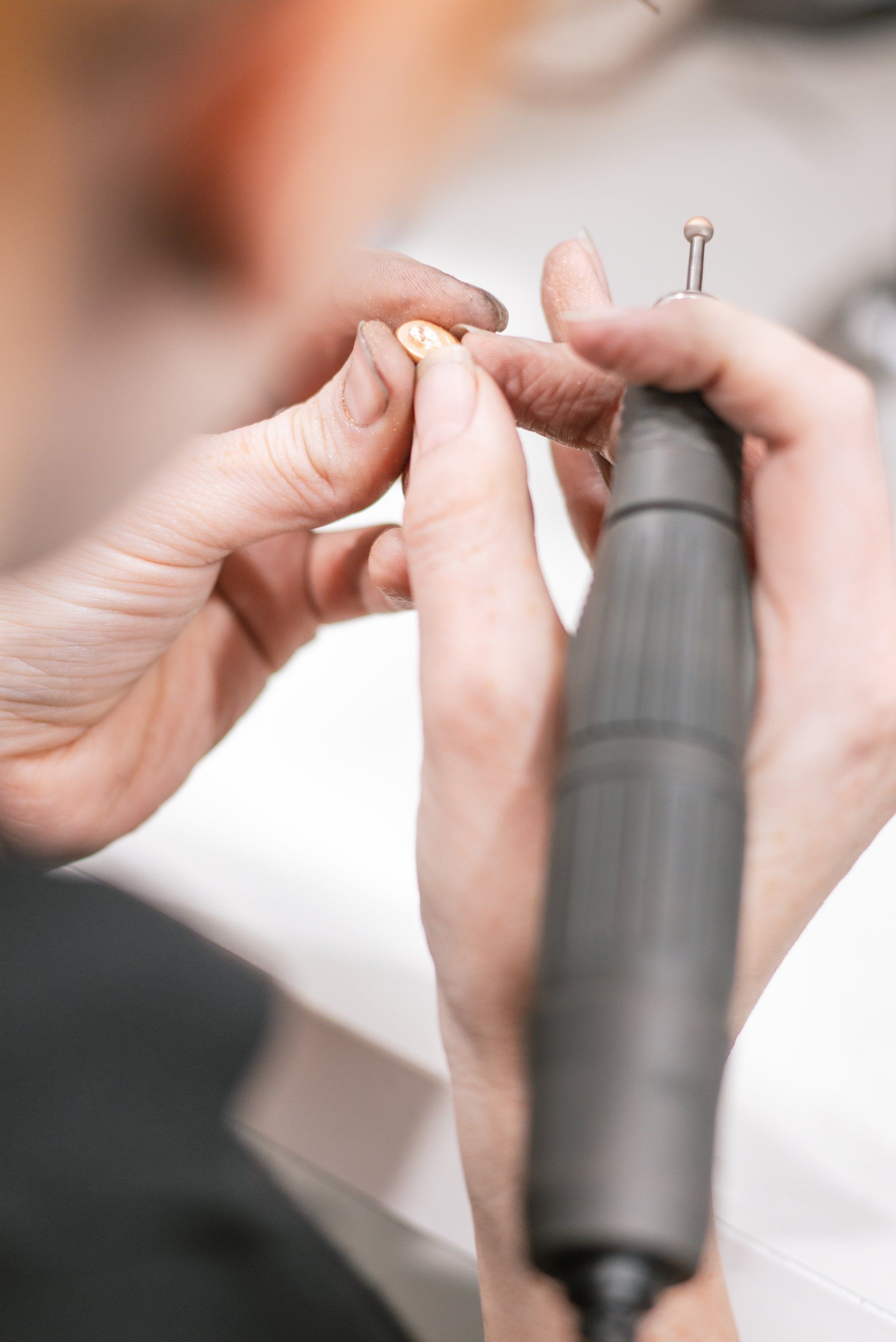 Close-up of hands using a nail drill on a fingernail in a manicure setting