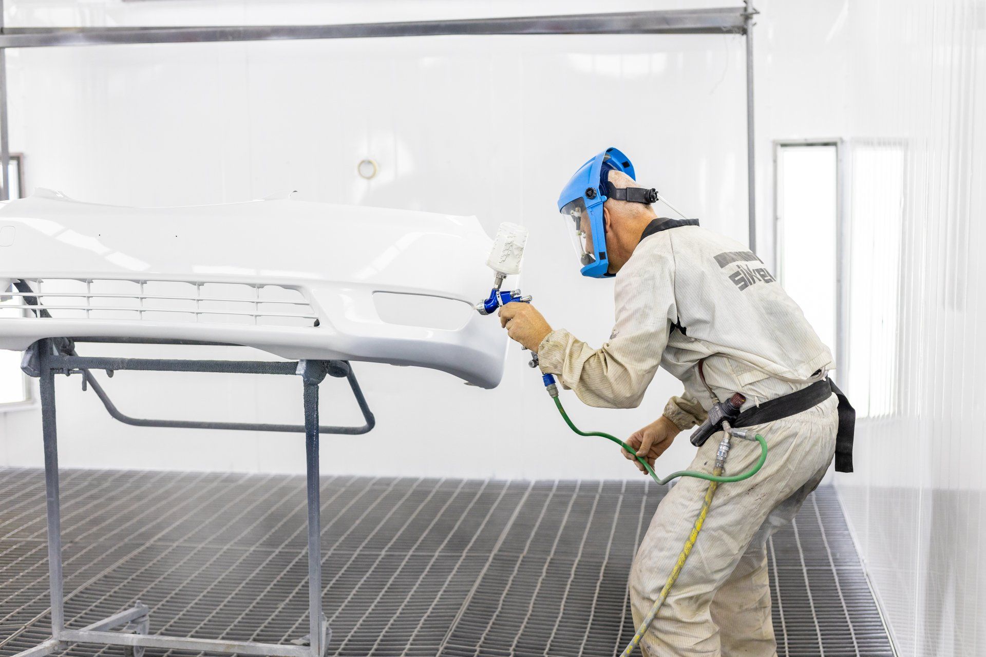 Worker spray-painting a white car body in a bright auto paint booth