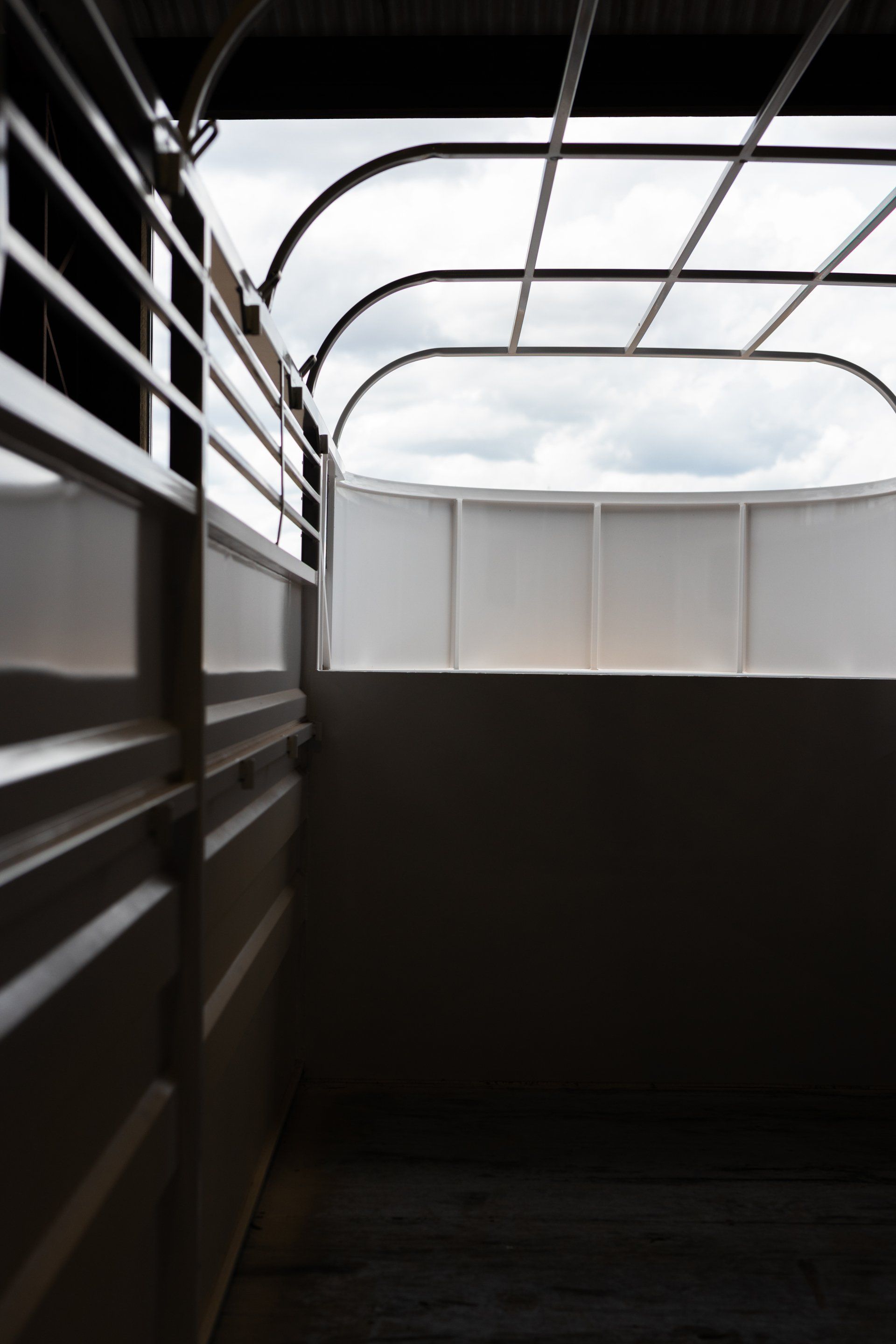 Empty livestock trailer interior with metal rails and a tarp roof, lit by daylight