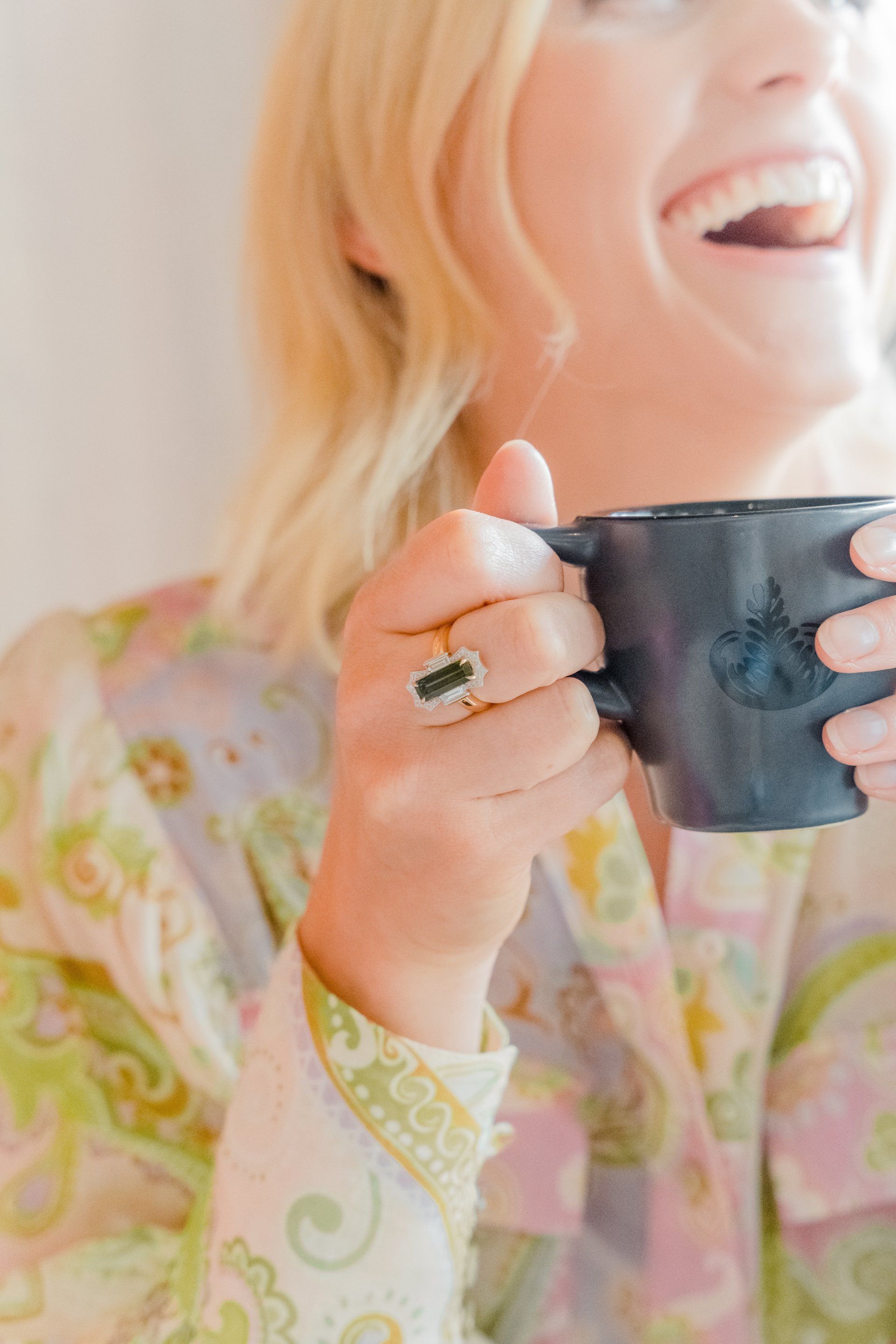 Person smiling and holding a dark mug, wearing a pastel patterned blouse.