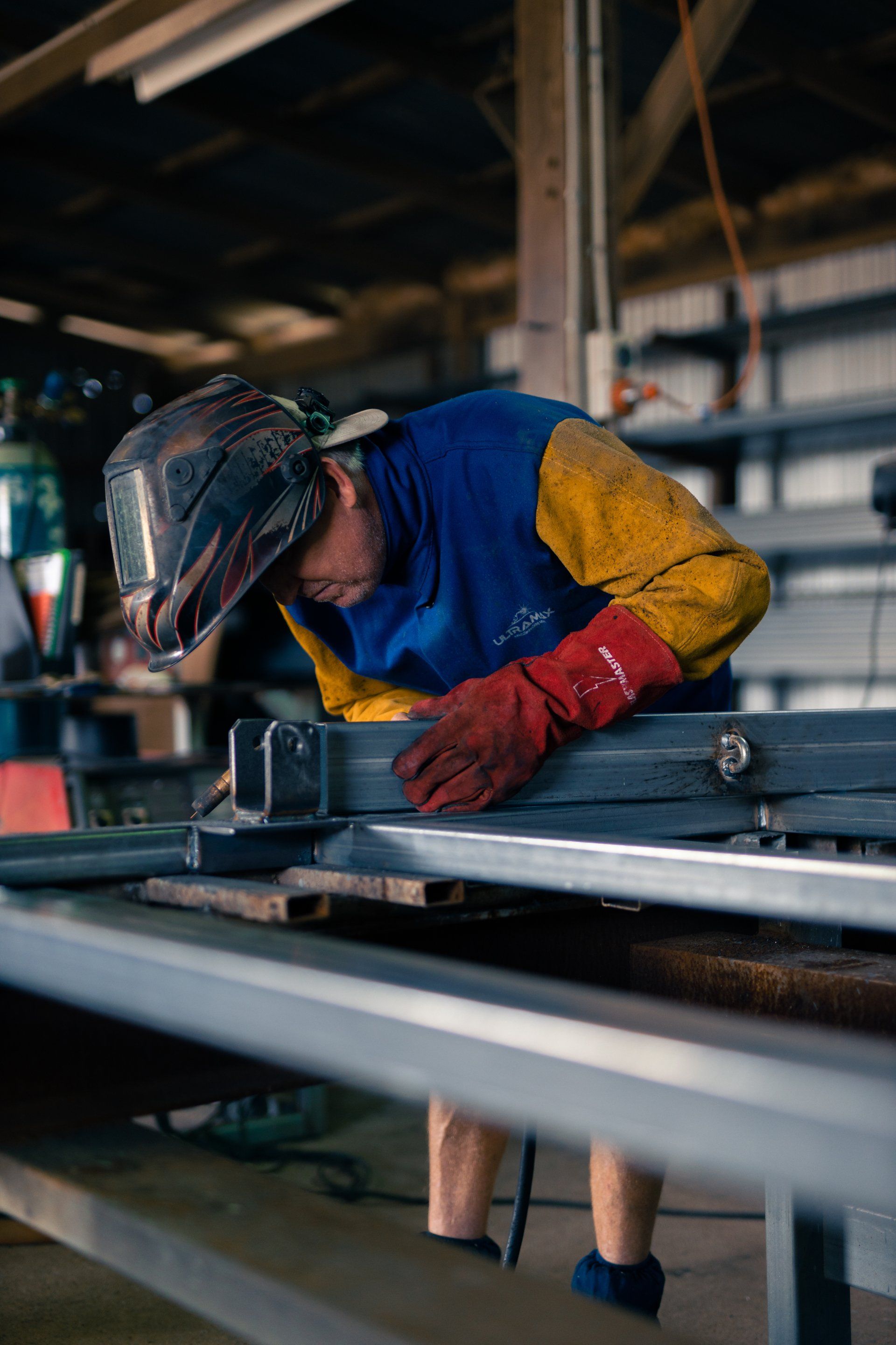 Welder in blue and yellow protective gear working on metal beams in a workshop
