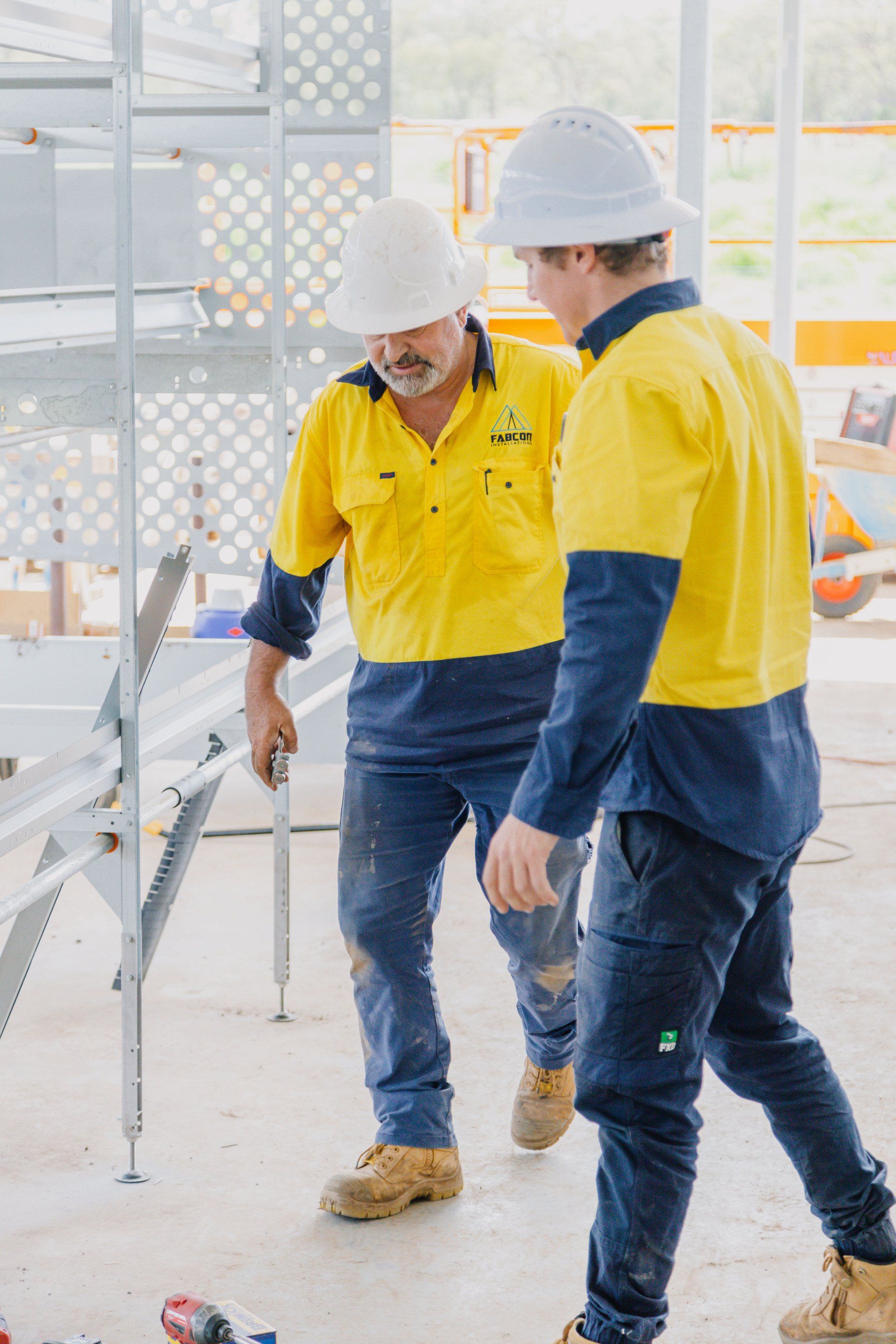 Two construction workers in hard hats and yellow shirts walking at an indoor worksite