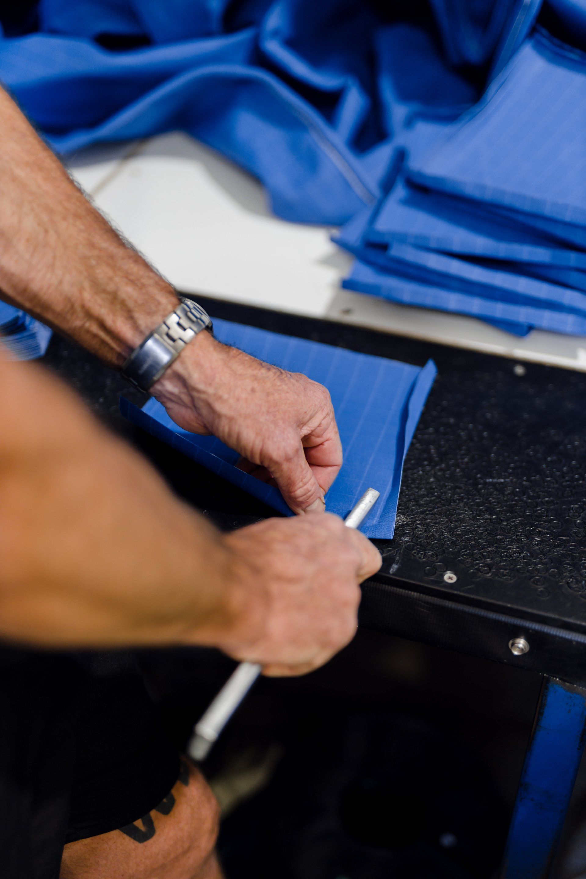 Hands folding a blue fabric garment on a worktable