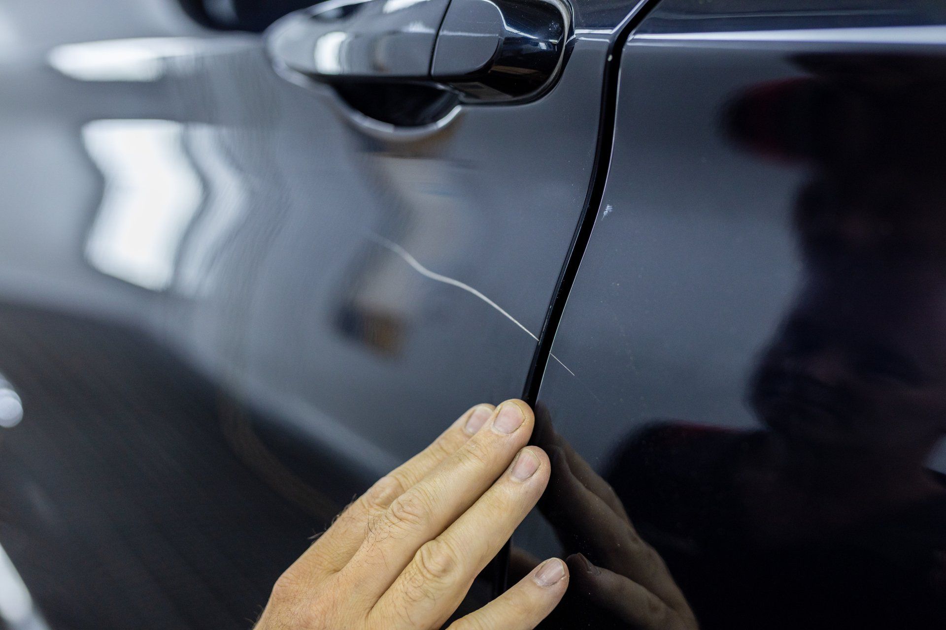 Hand checking a dark car door for dents or scratches, with the reflection visible in the paint.