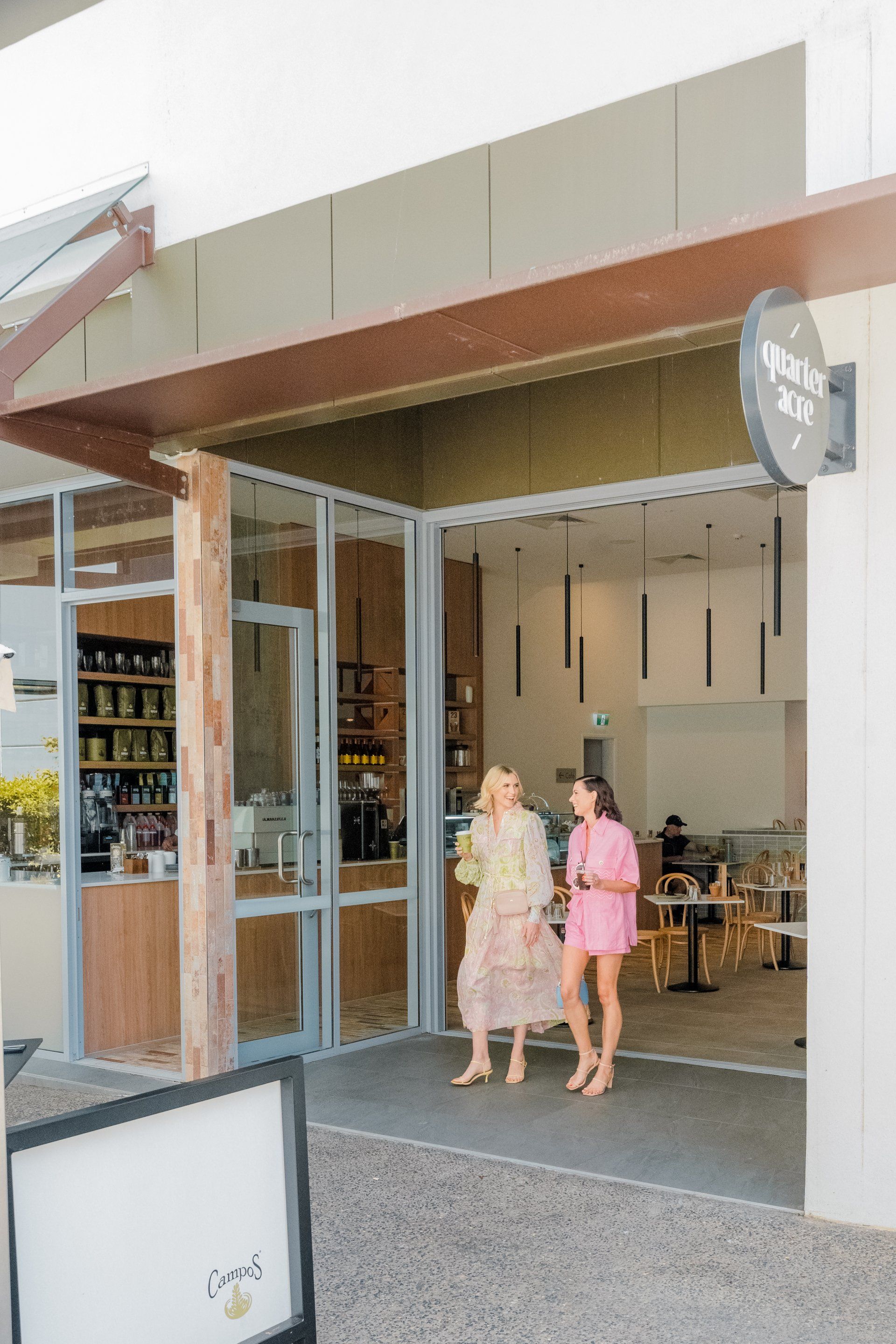 Two people walking into a cafe with a glass storefront and wooden awning