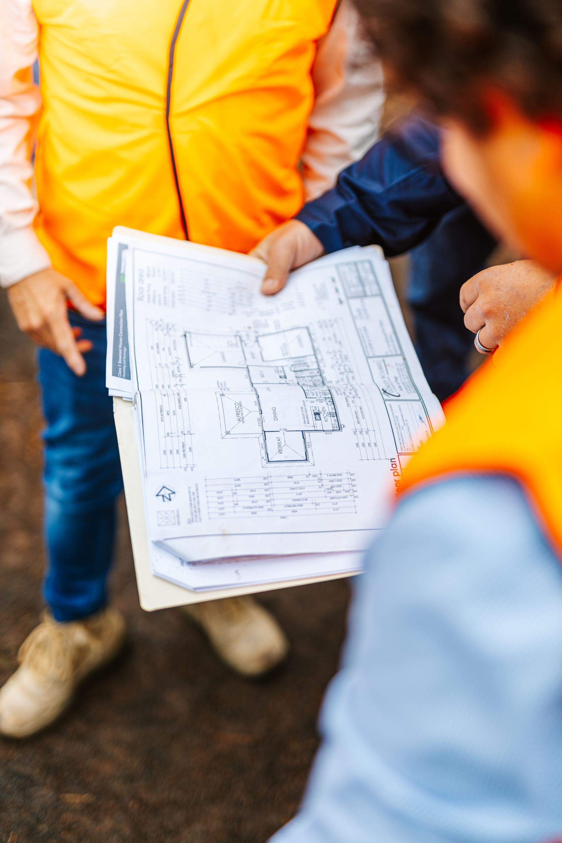 People in orange safety vests reviewing construction plans outdoors