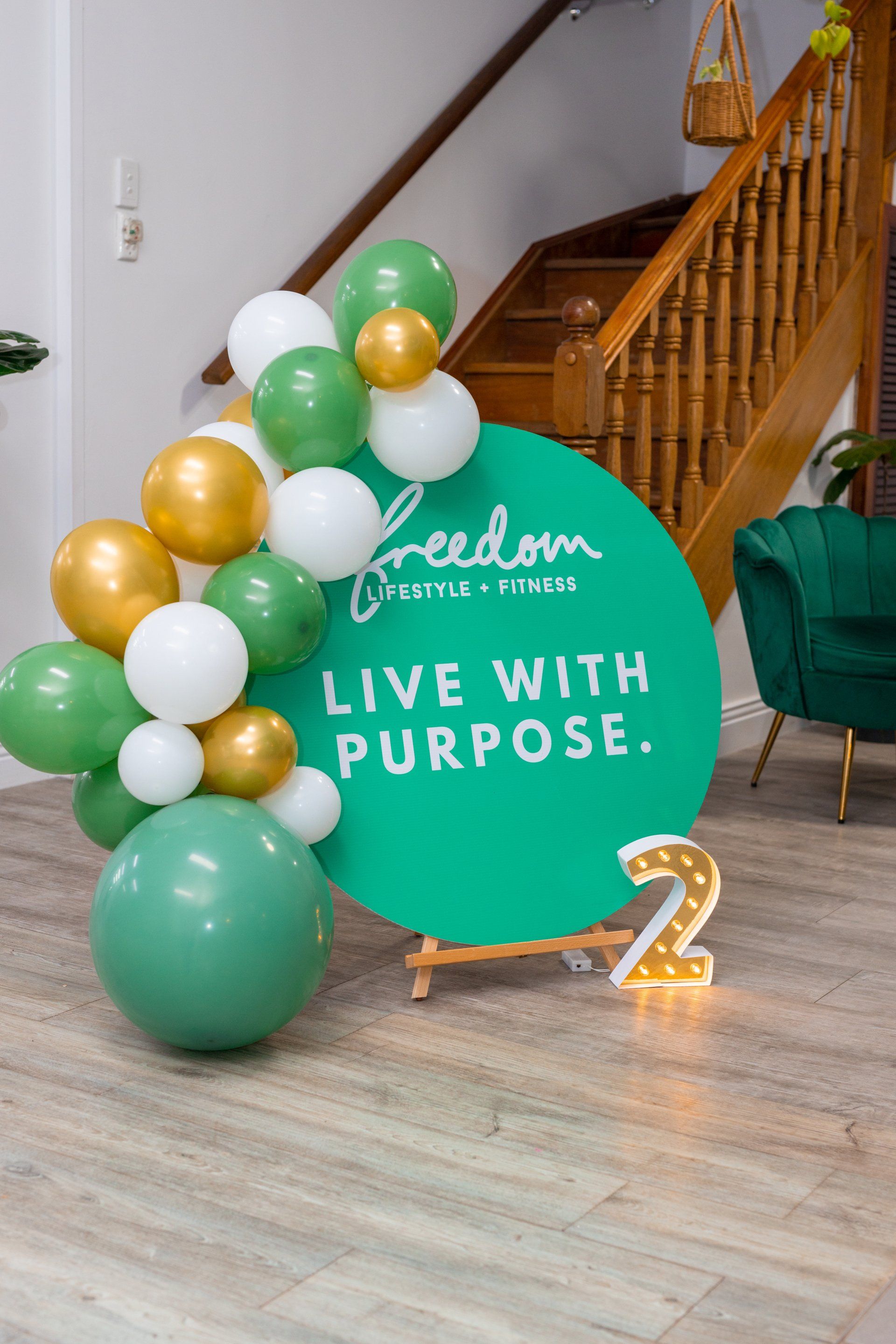 Green and white balloon display beside a teal sign reading “Live with Purpose” in a decorated room