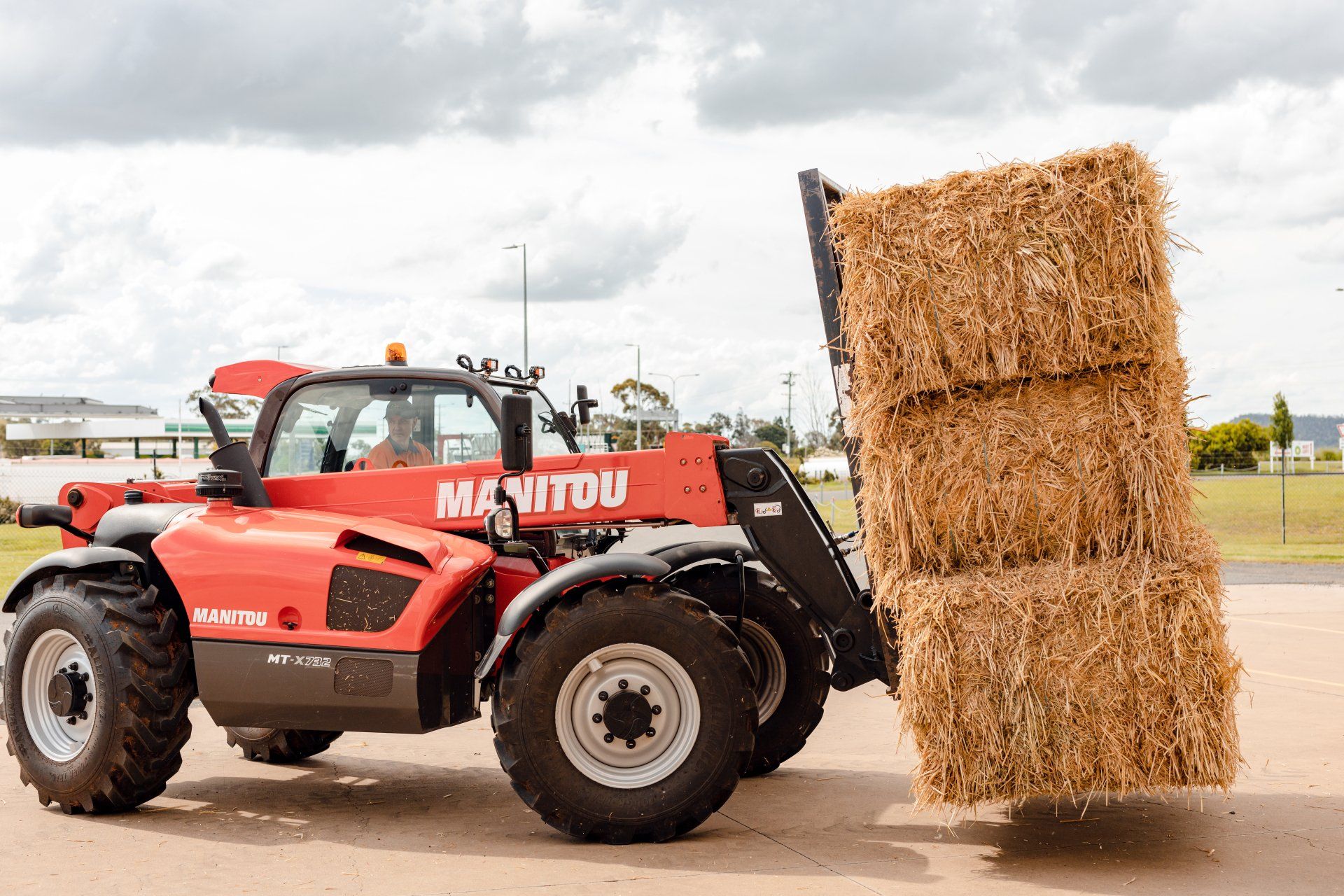 Red telehandler lifting stacked hay bales in an open farmyard