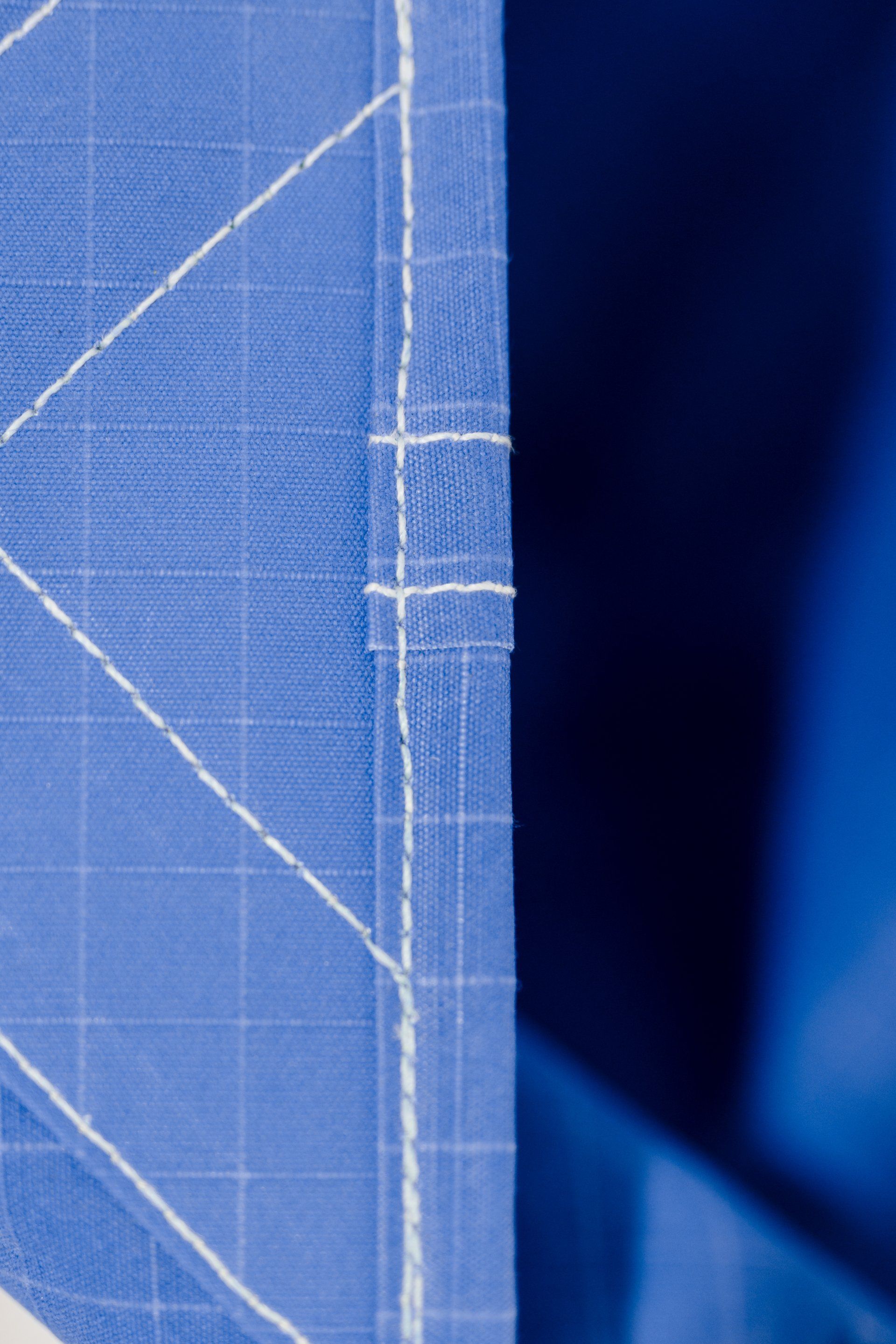 Close-up of blue patterned fabric with white stitched seams and a dark blue background