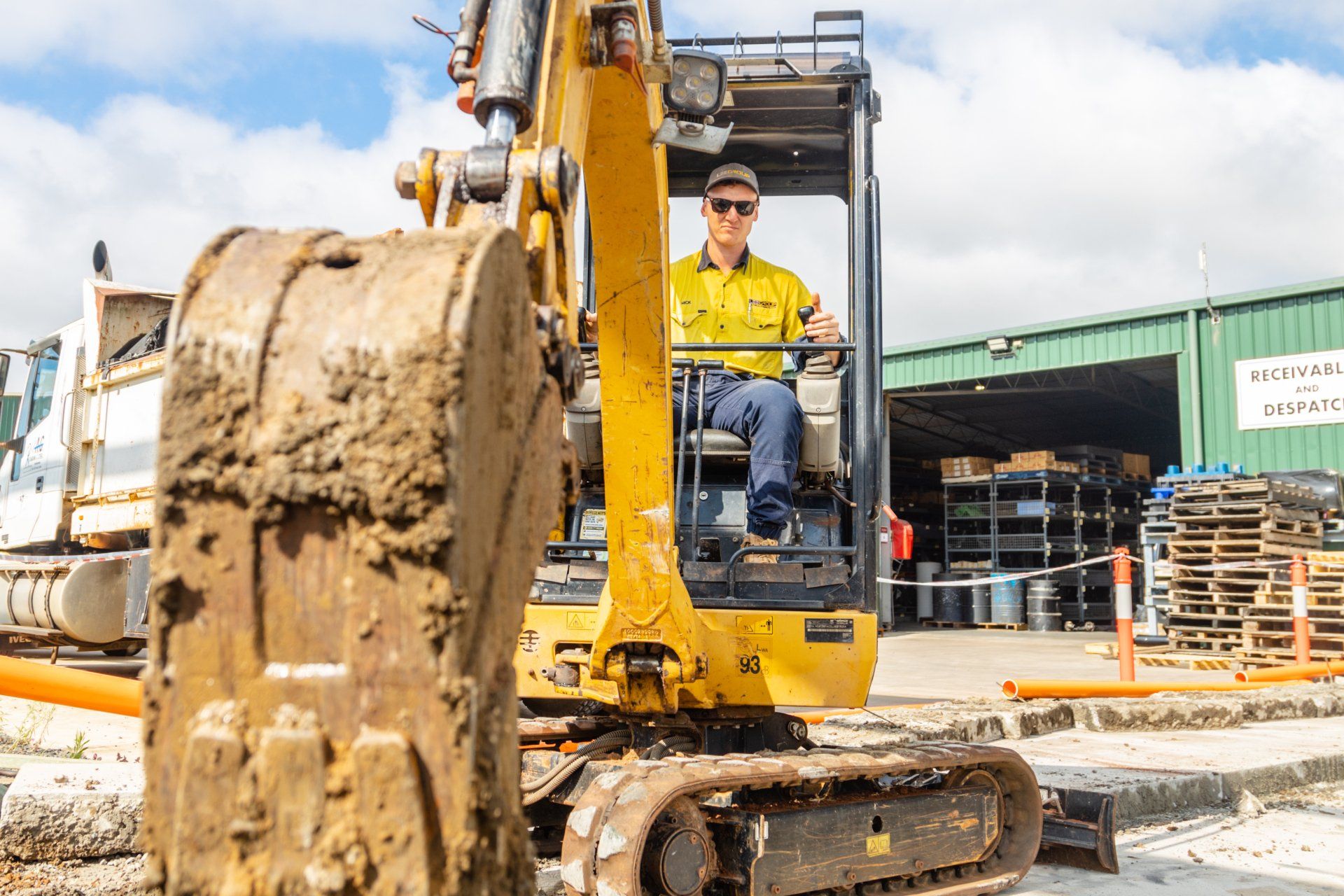 Yellow excavator at a construction site with a worker in the cab, muddy bucket in foreground