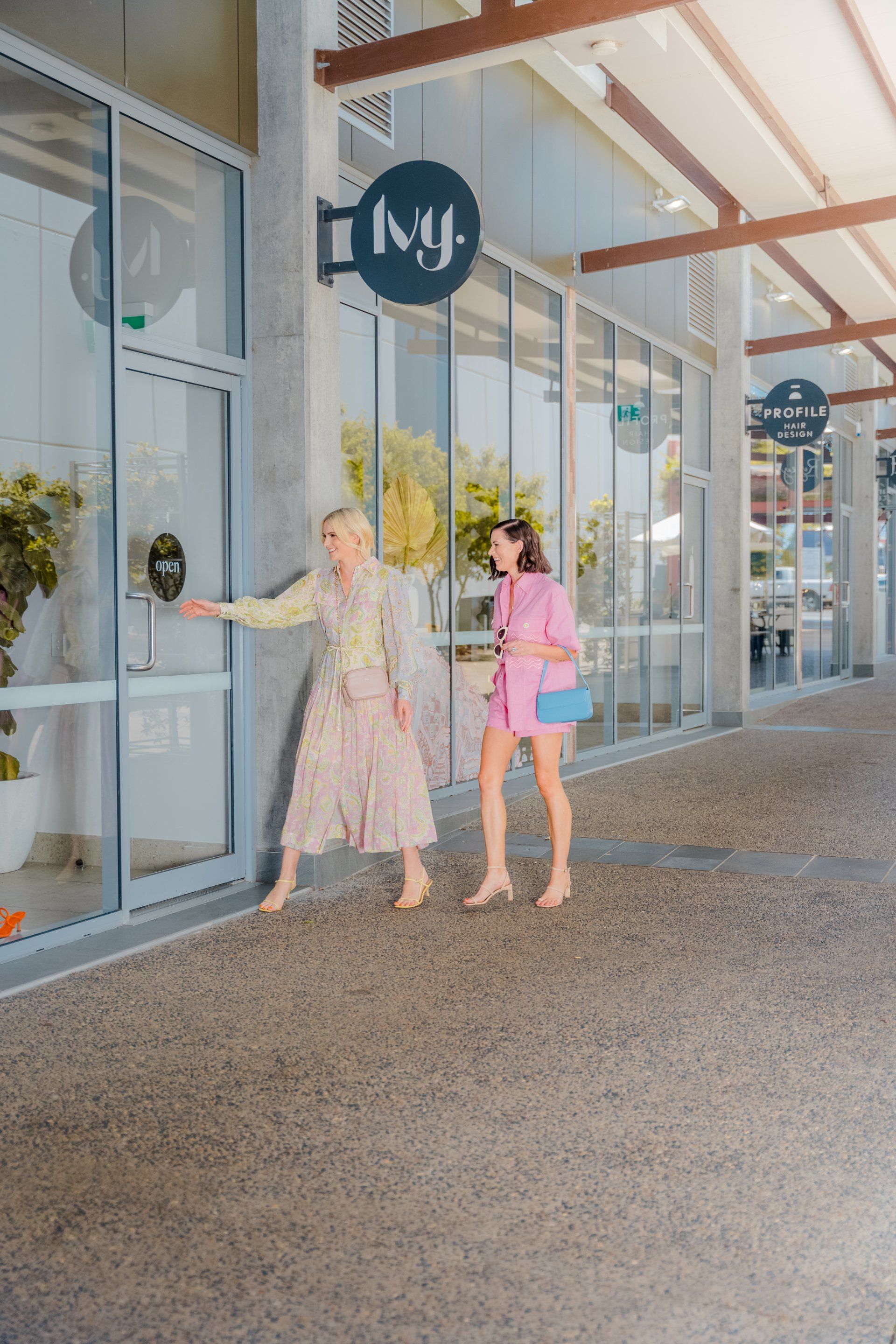 Two women walking past storefronts under a covered outdoor walkway, one opening a door