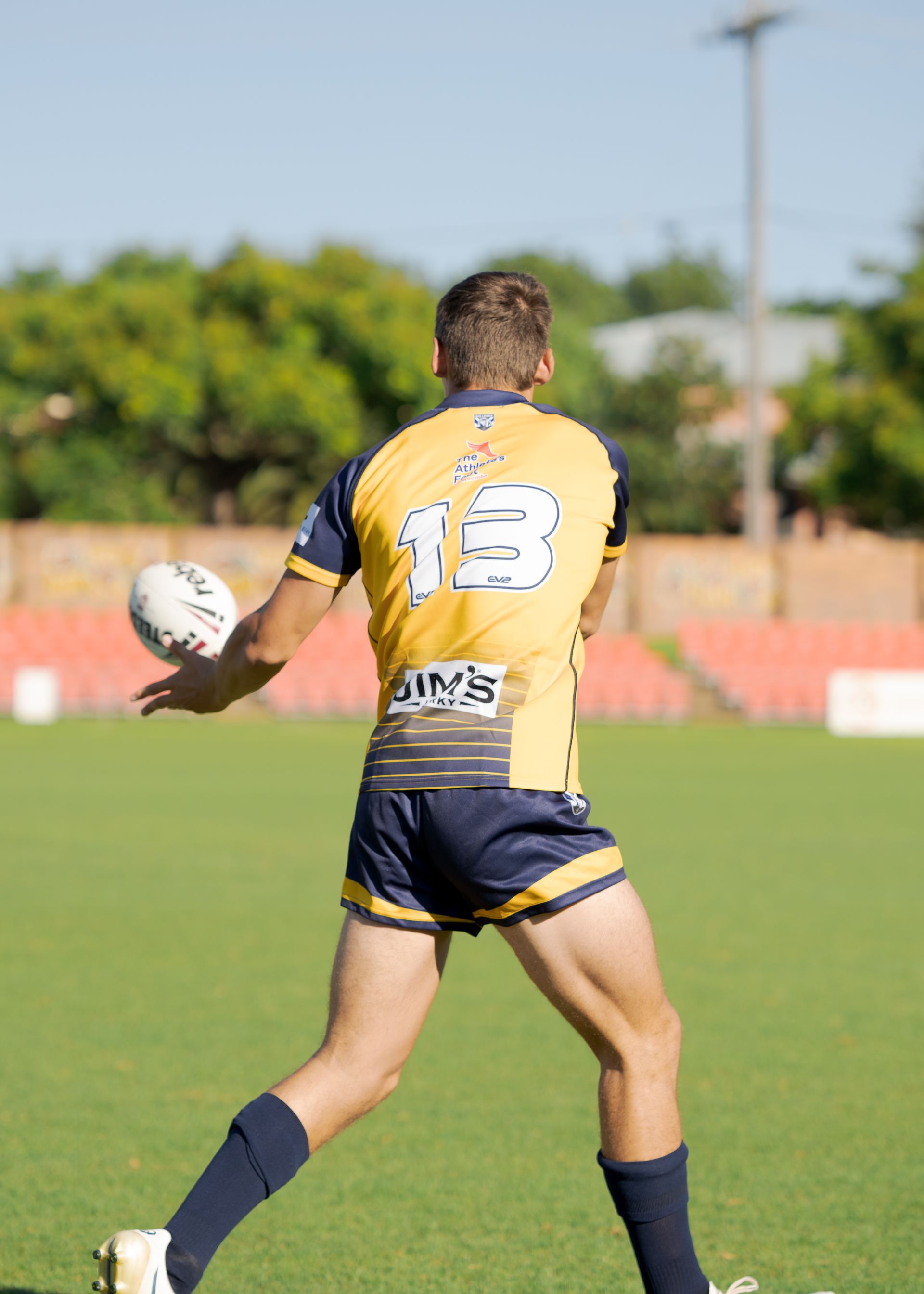 Rugby player in yellow jersey with number 18 runs holding a ball on a grassy field.