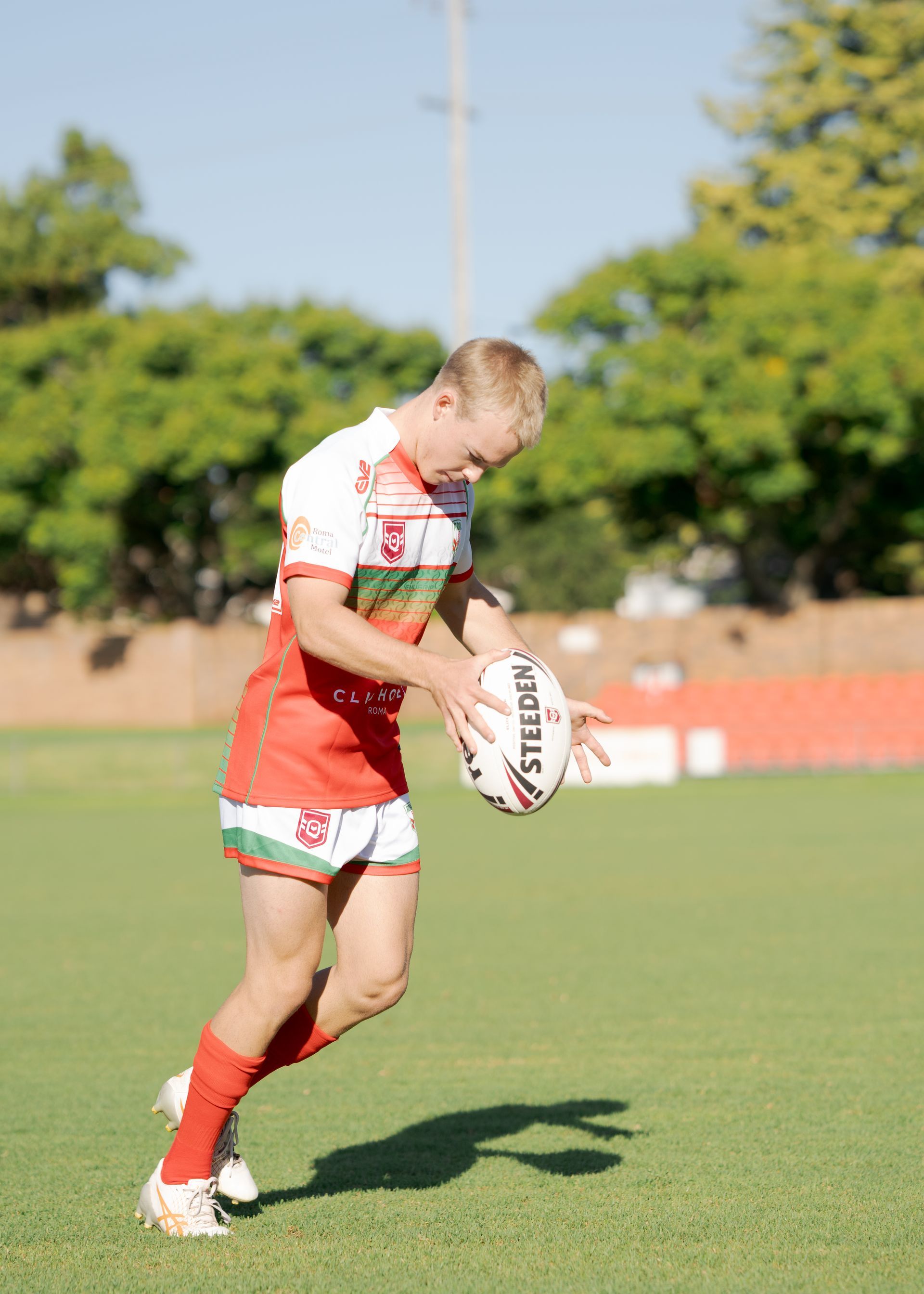 Rugby player in red and white uniform holding a ball on a grassy field