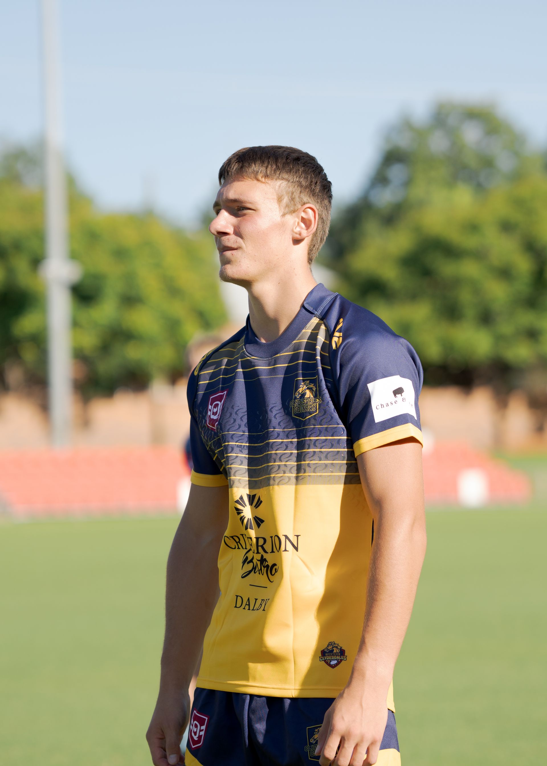 Soccer player in blue and yellow jersey standing on a field, looking to the side.