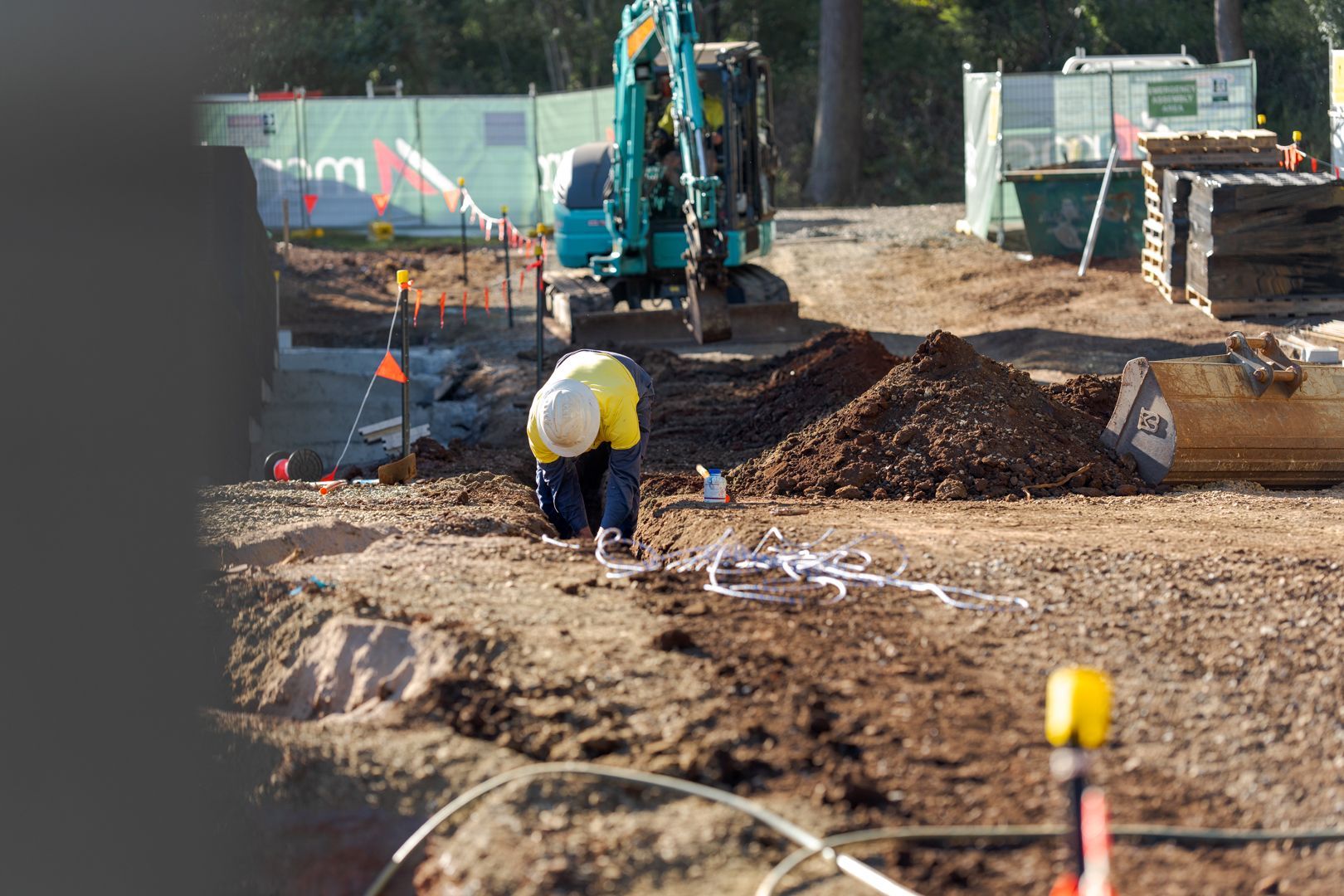 Construction workers digging a trench with an excavator at a muddy roadwork site