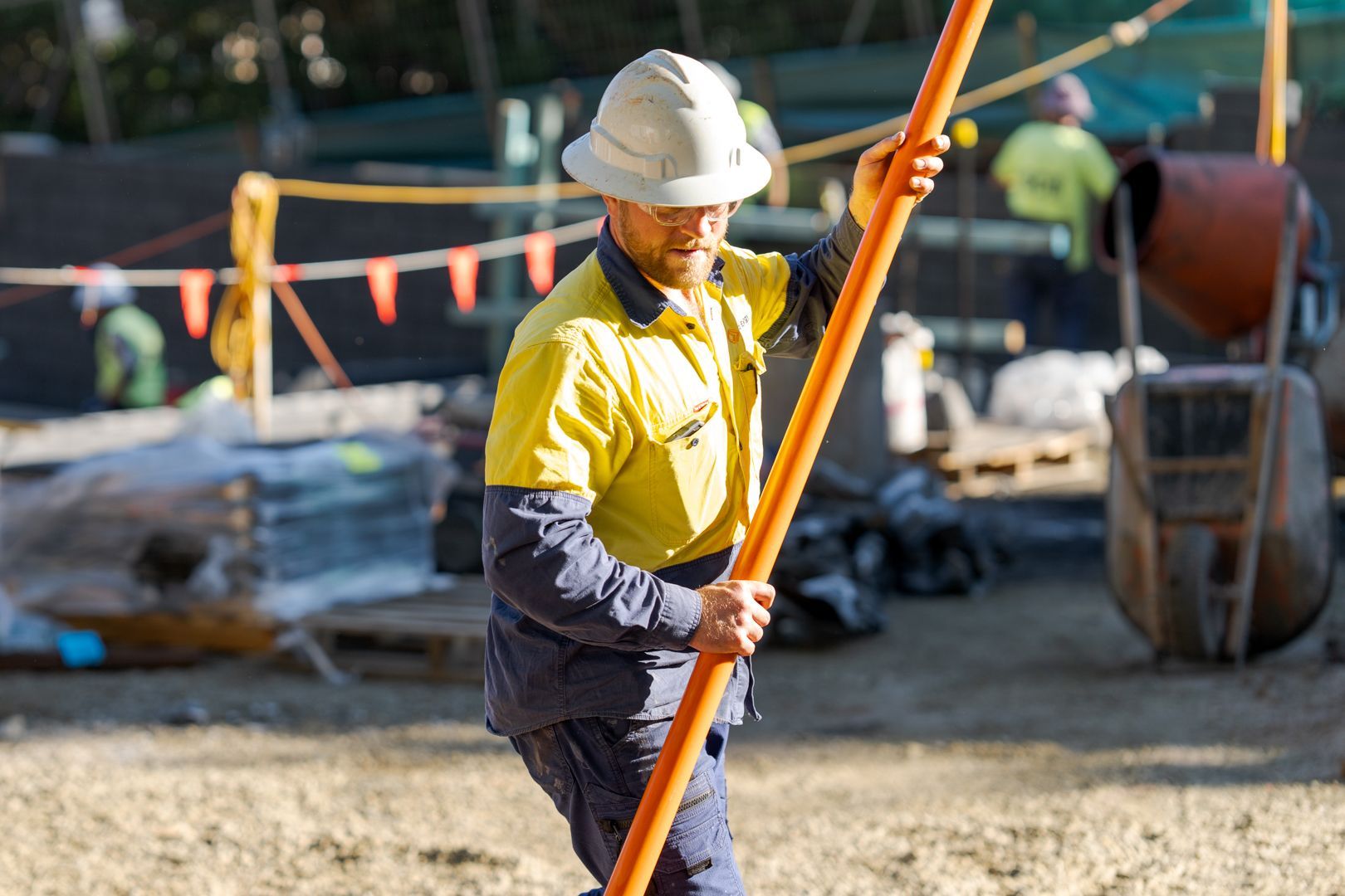 Construction worker in a hard hat holding an orange surveying rod at a worksite