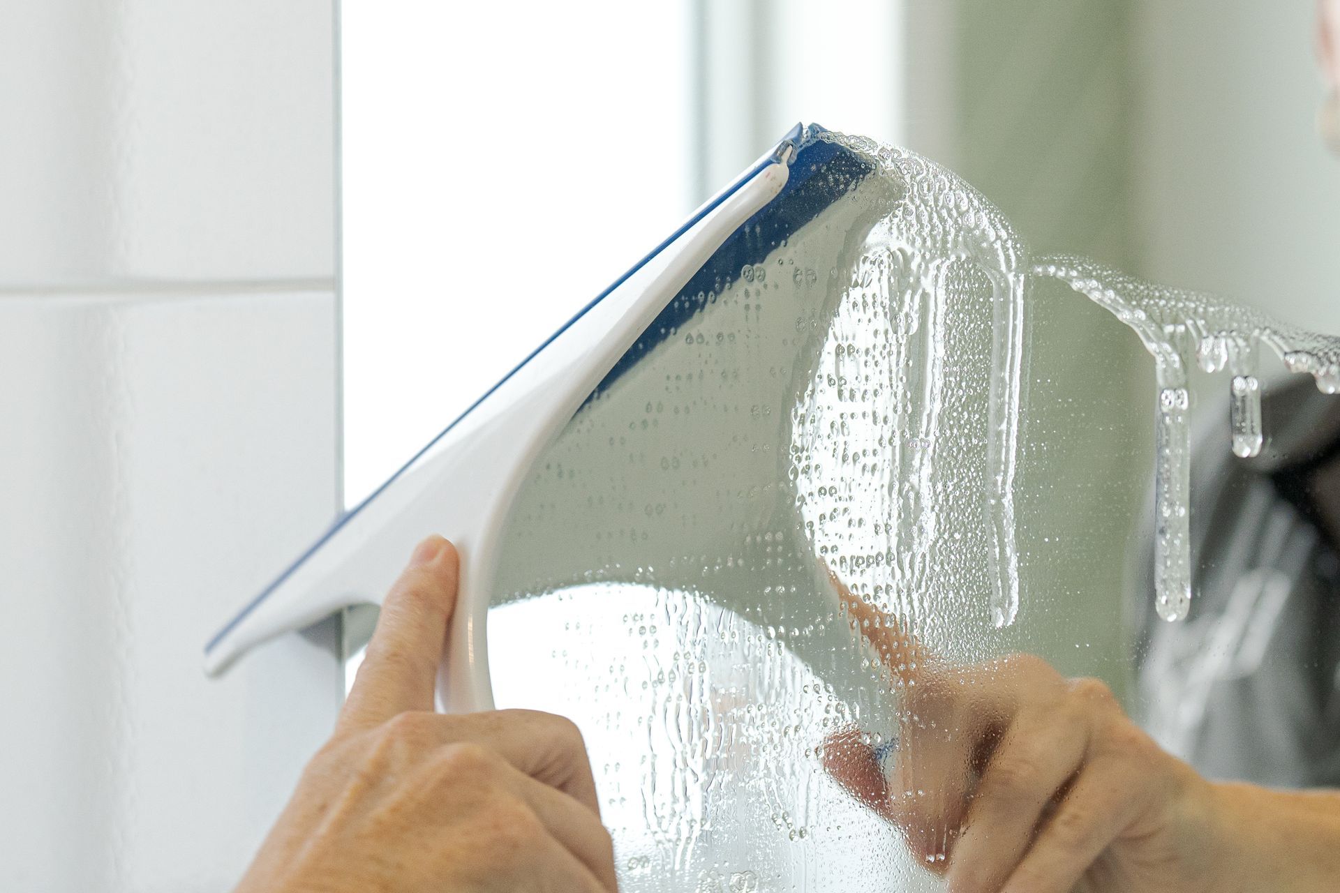 Hands using a squeegee to clean a window with water and soap suds