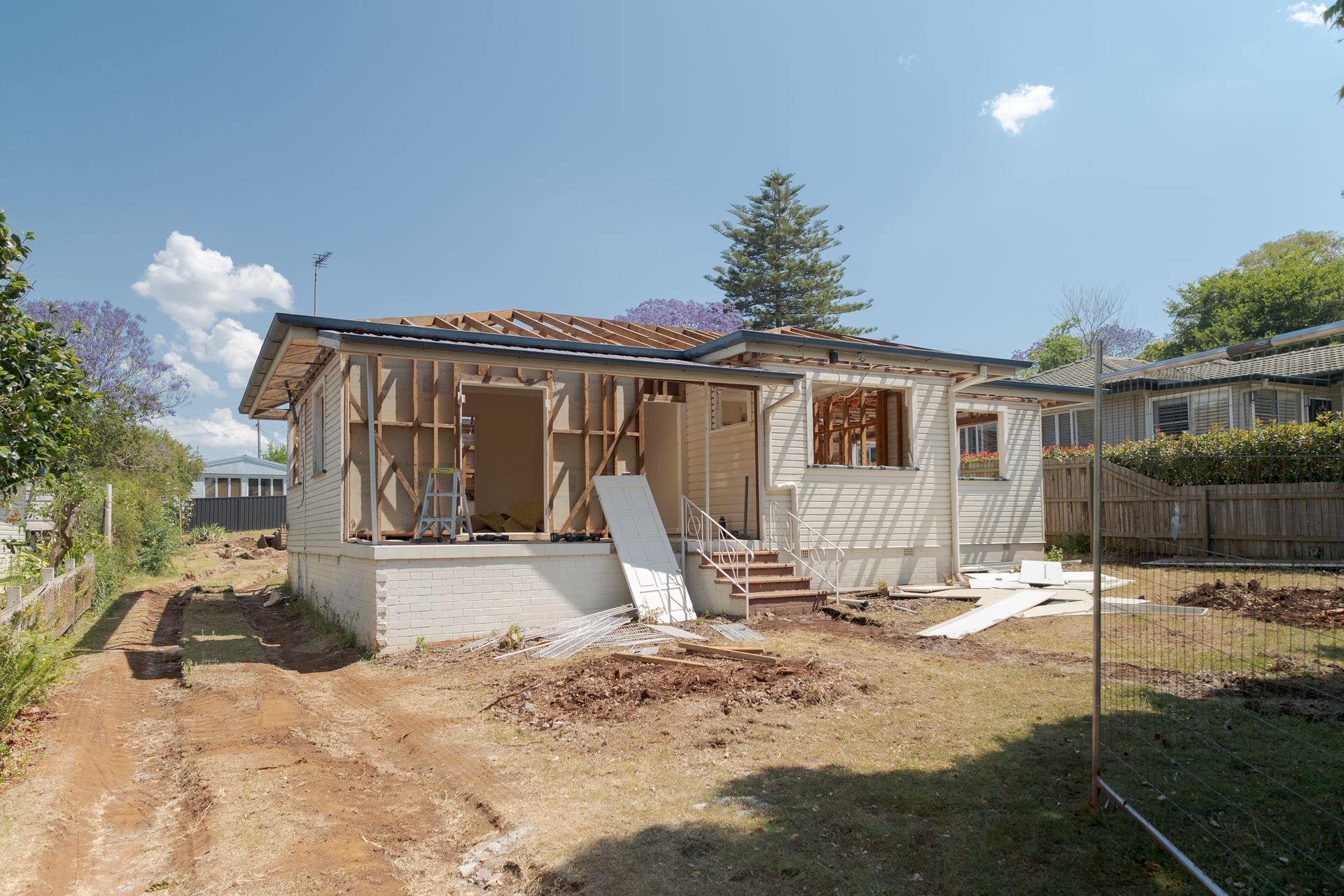 Partially demolished house under renovation with exposed framing, debris, and blue sky