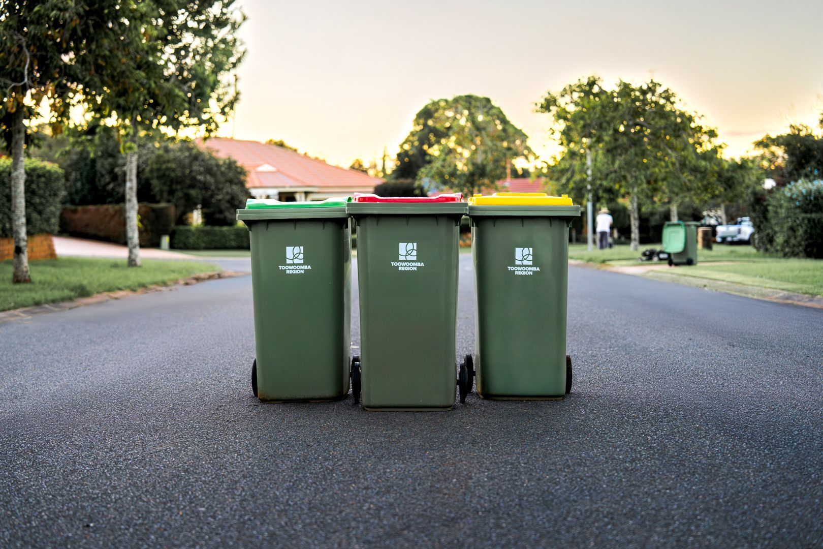 Three green garbage bins on a suburban street at dusk