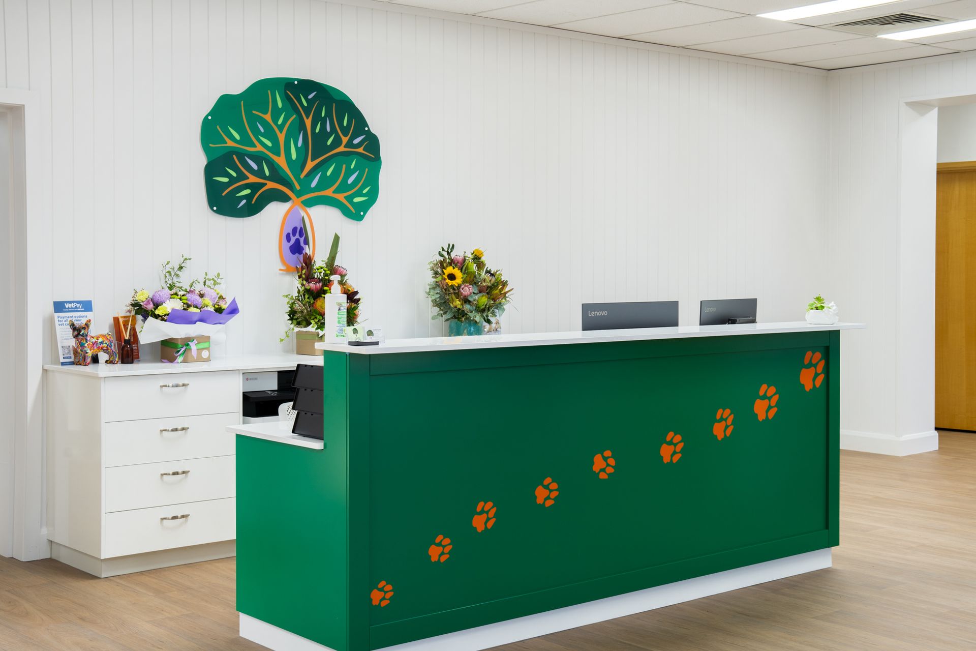 Modern reception desk with green front, white walls, and decorative tree wall art in a bright lobby