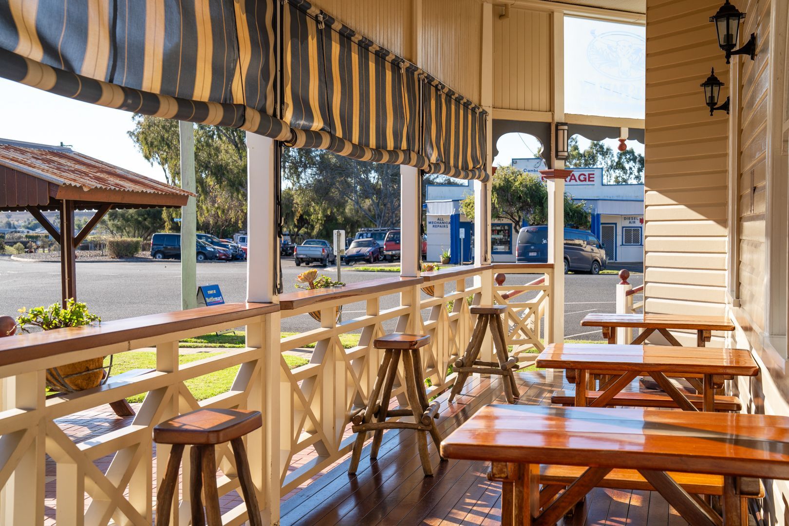 Sunlit outdoor café patio with wooden tables, stools, and striped awning overlooking a street