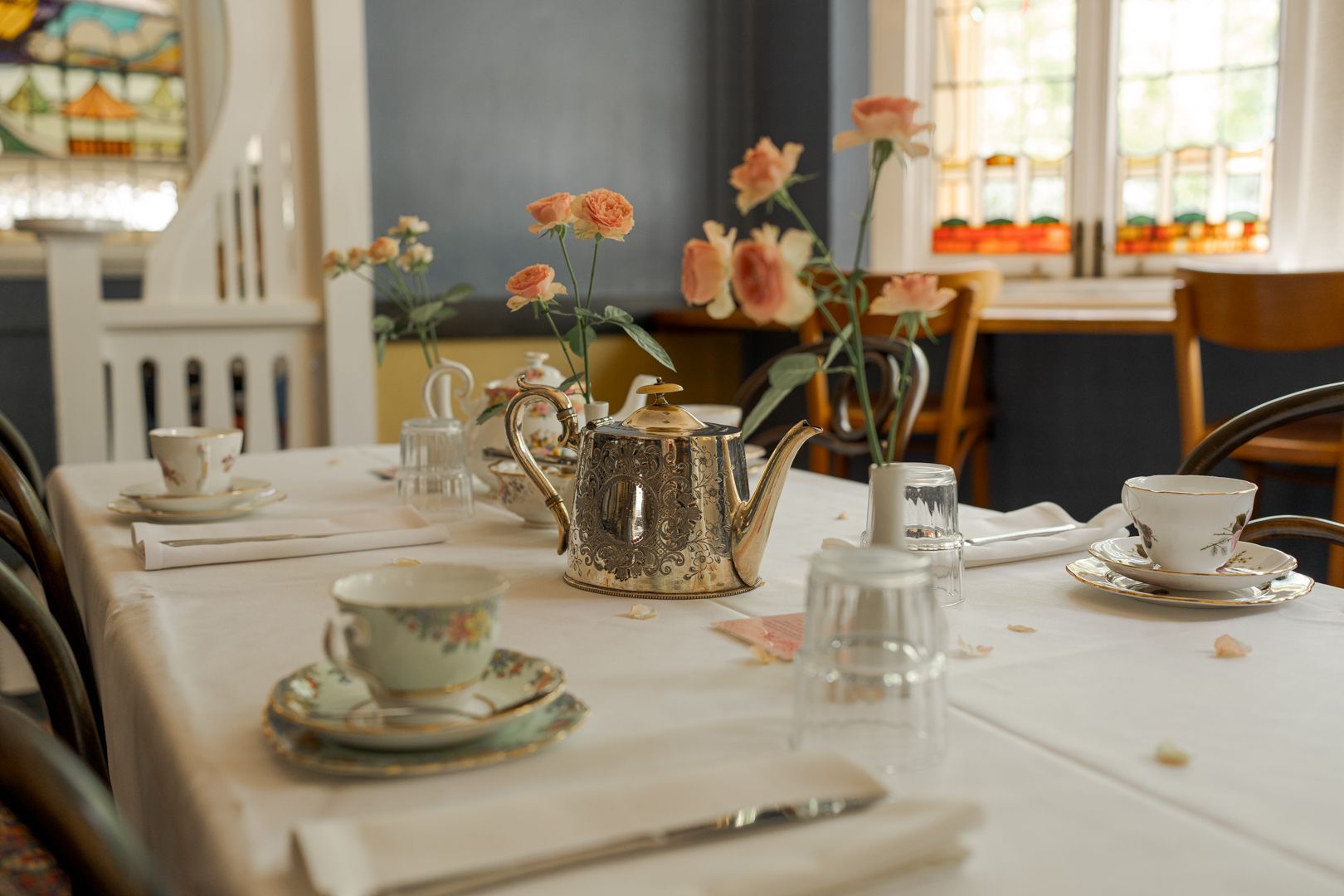 Tea set and pink flowers on a white dining table in a bright room with stained glass windows