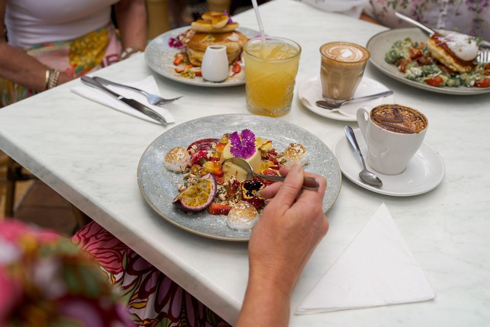 Person serving plated dessert at a white-clothed table with drinks and teacups
