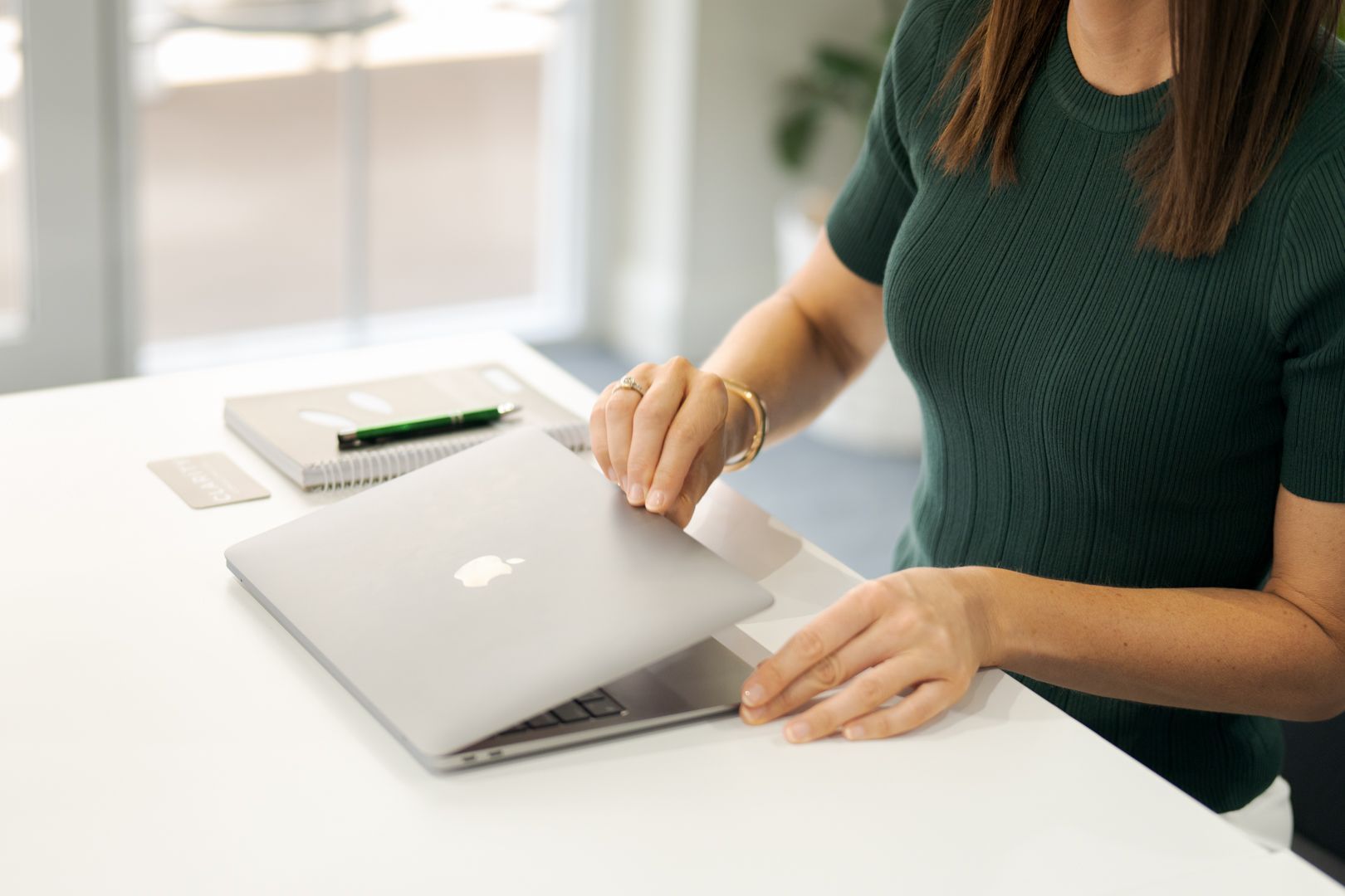 Person opening a silver laptop on a white desk in a bright office