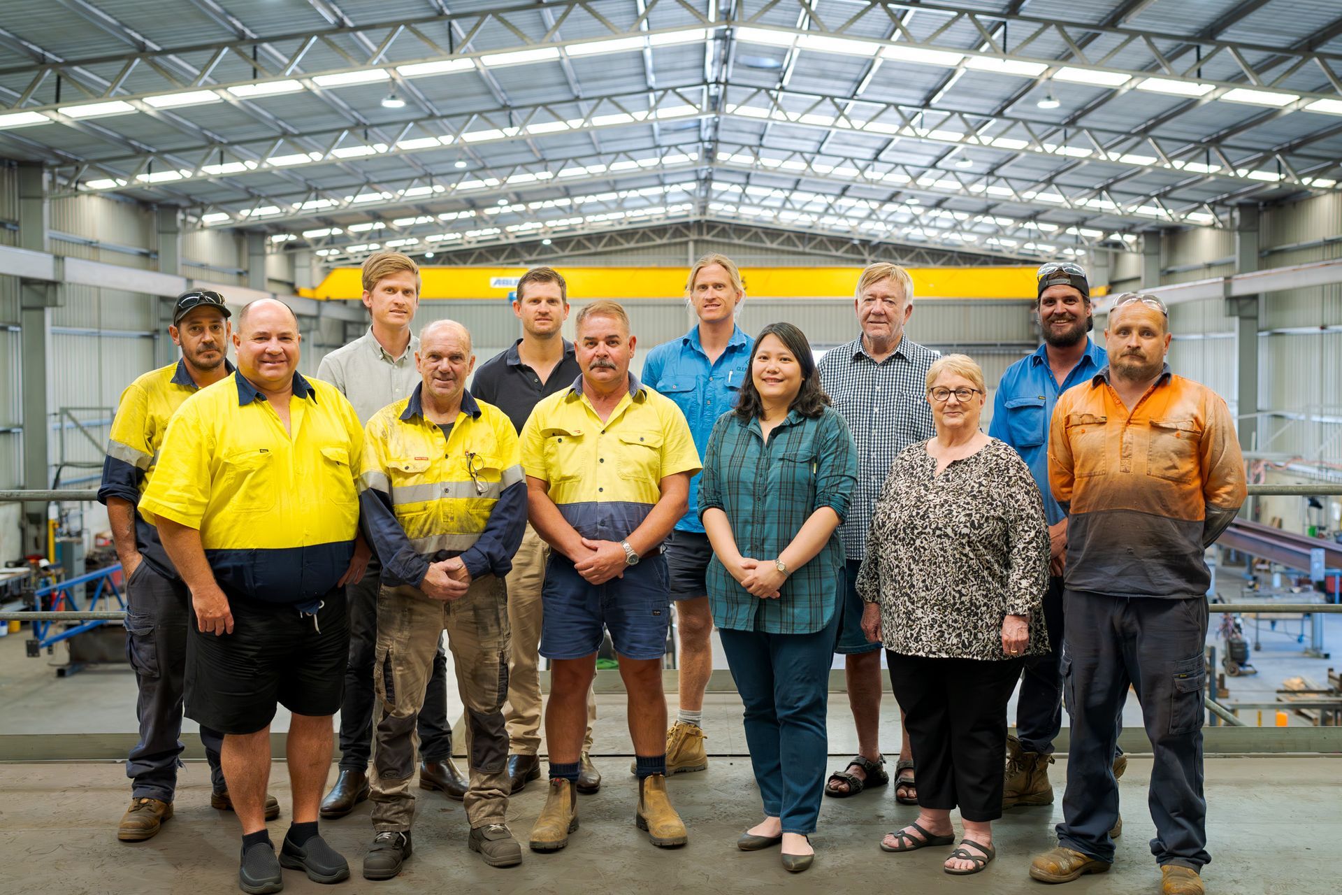 Group of workers standing in a factory, with bright yellow shirts and machinery in the background.