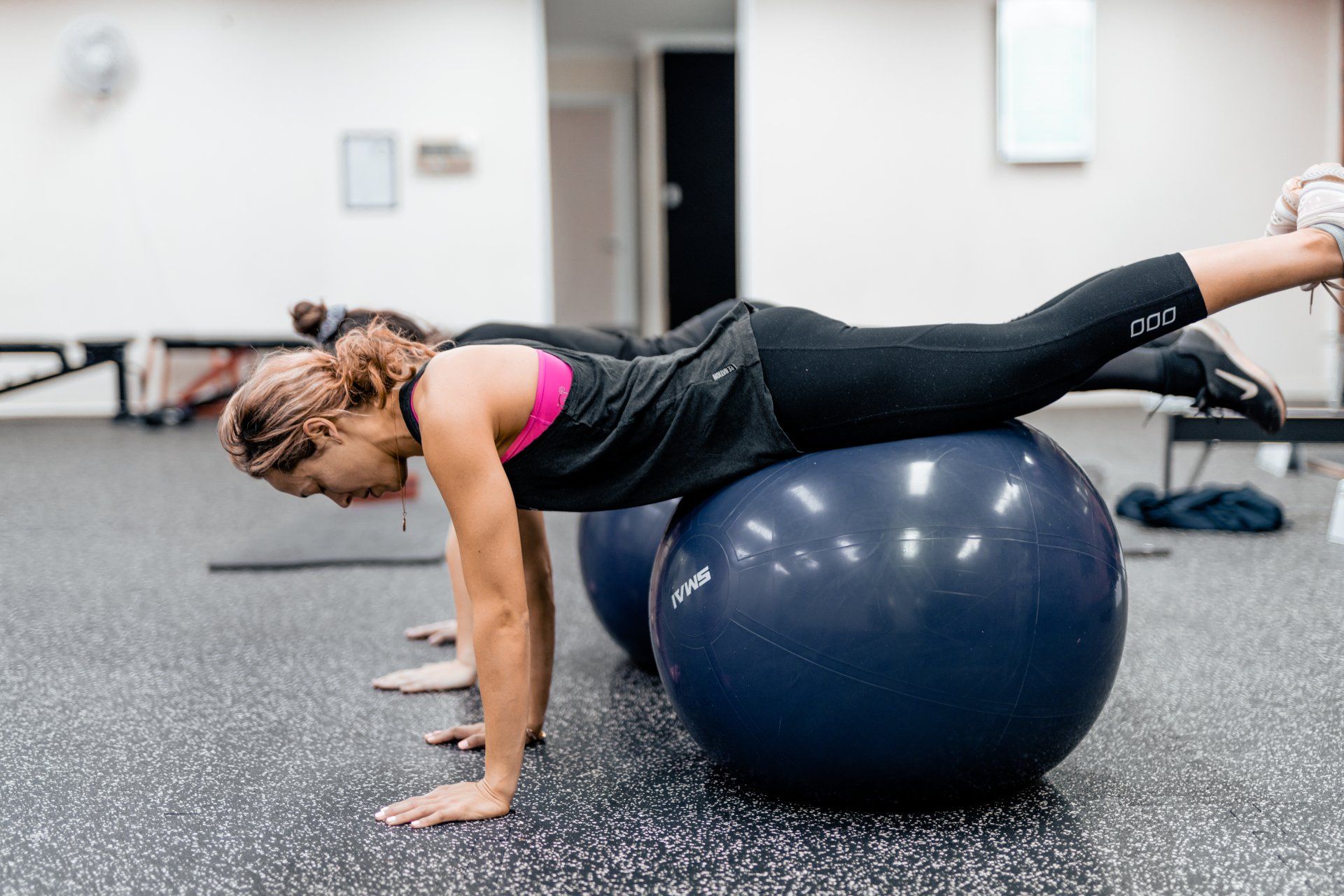 Woman exercising on a blue stability ball in a gym, holding a plank position.