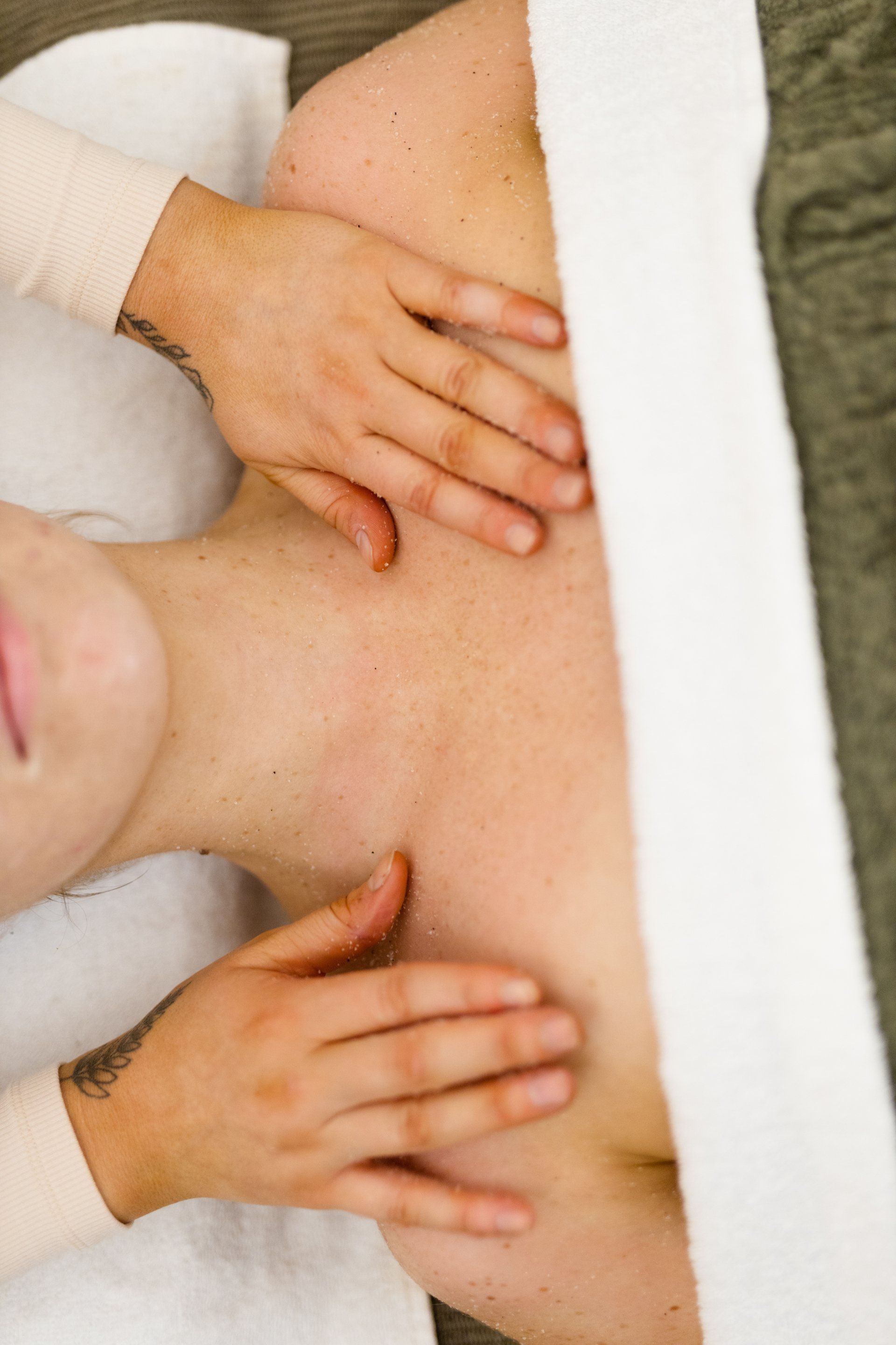 Hands massaging a person’s bare back with oil on a white towel.