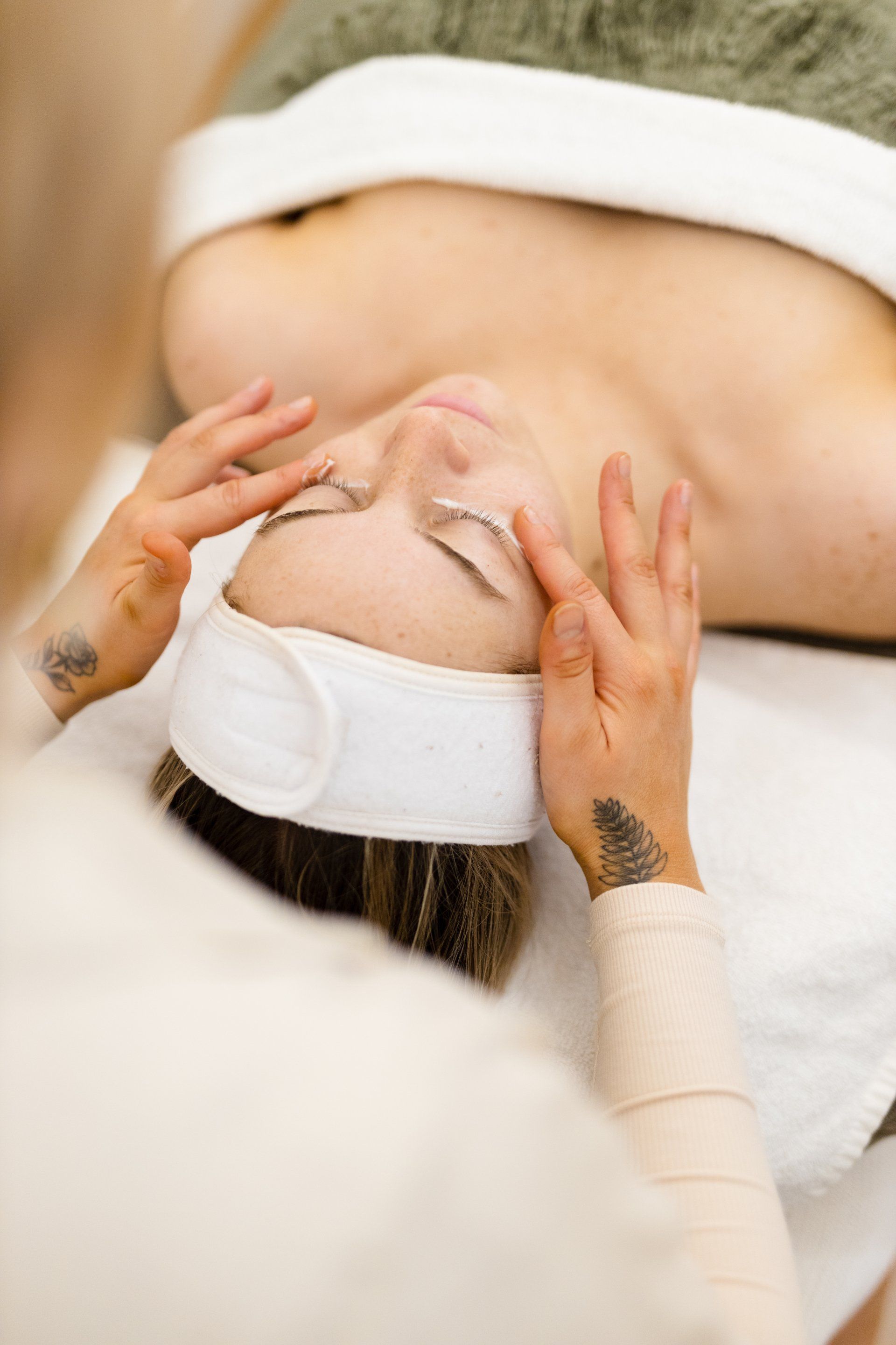 Person receiving a facial massage with a white headband, lying on a treatment bed