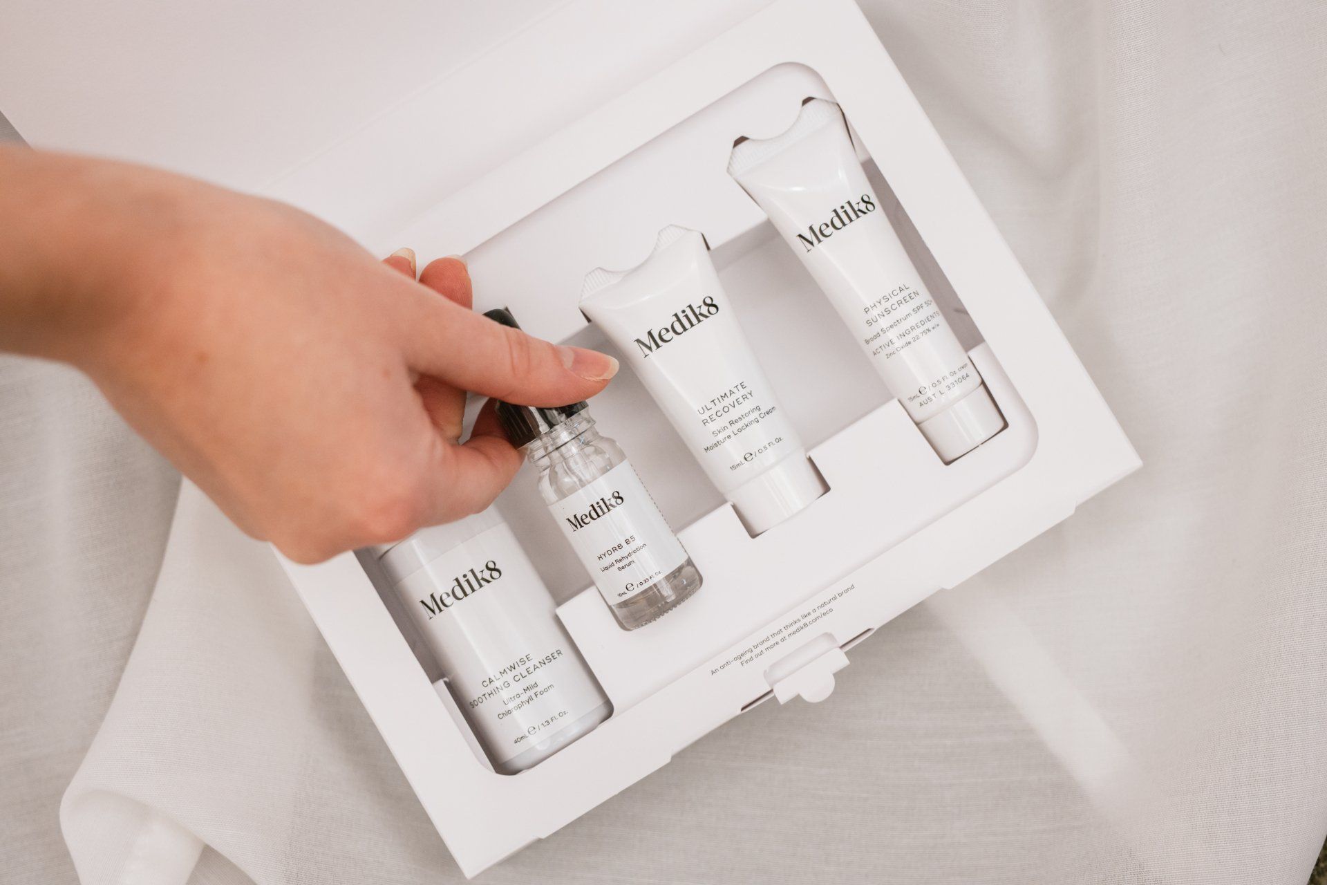 Hand placing white skincare bottles in a white gift box